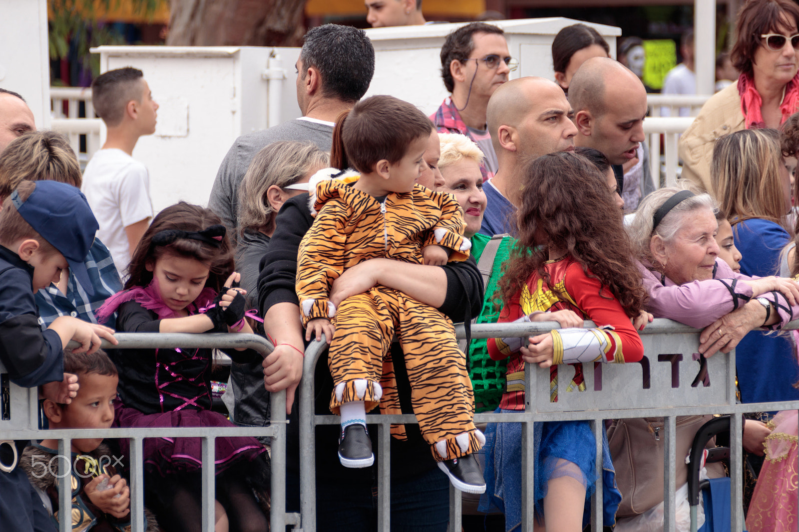 Canon EF 75-300mm F4.0-5.6 IS USM sample photo. Viewers from behind dividing fence look at the arnival parade photography