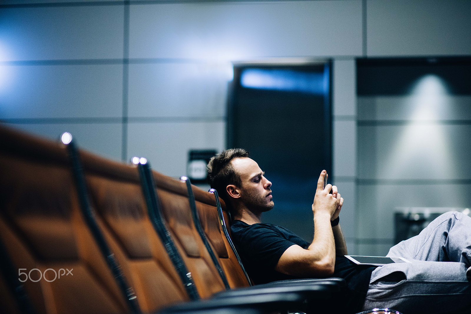 Canon EOS 5DS + Canon EF 85mm F1.8 USM sample photo. Young adult man waiting in airport lounge using smart phone photography