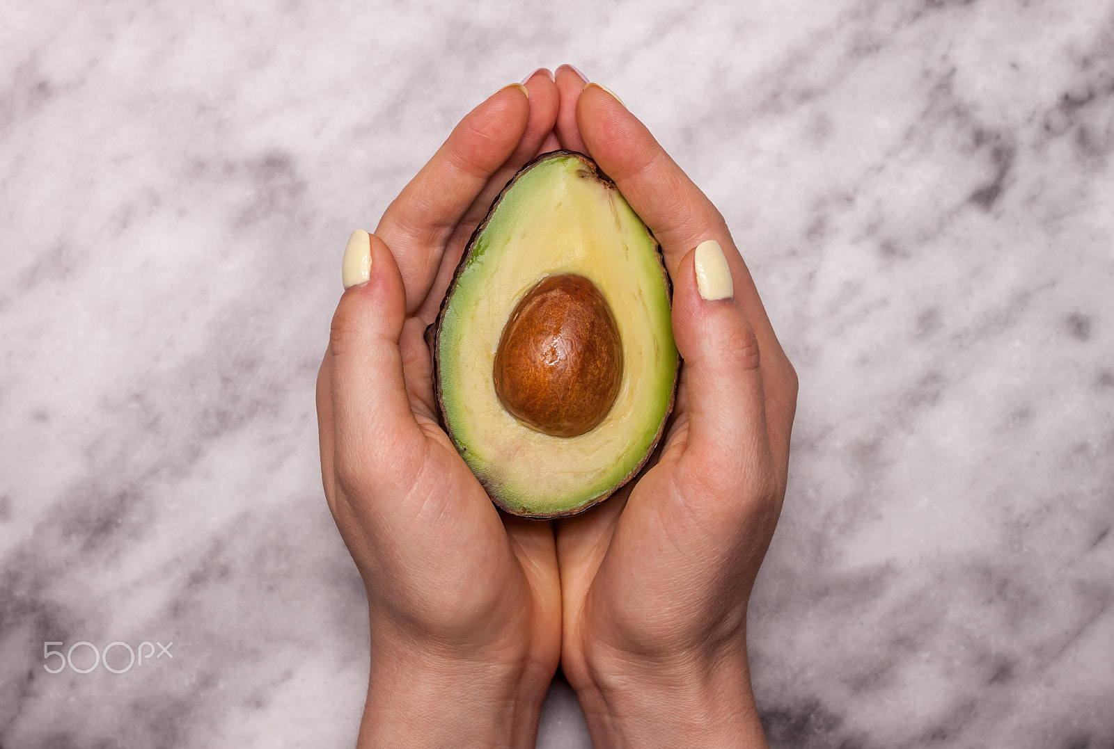 Canon EOS 500D (EOS Rebel T1i / EOS Kiss X3) + Canon EF 40mm F2.8 STM sample photo. Female hands keeping cut avocado photography