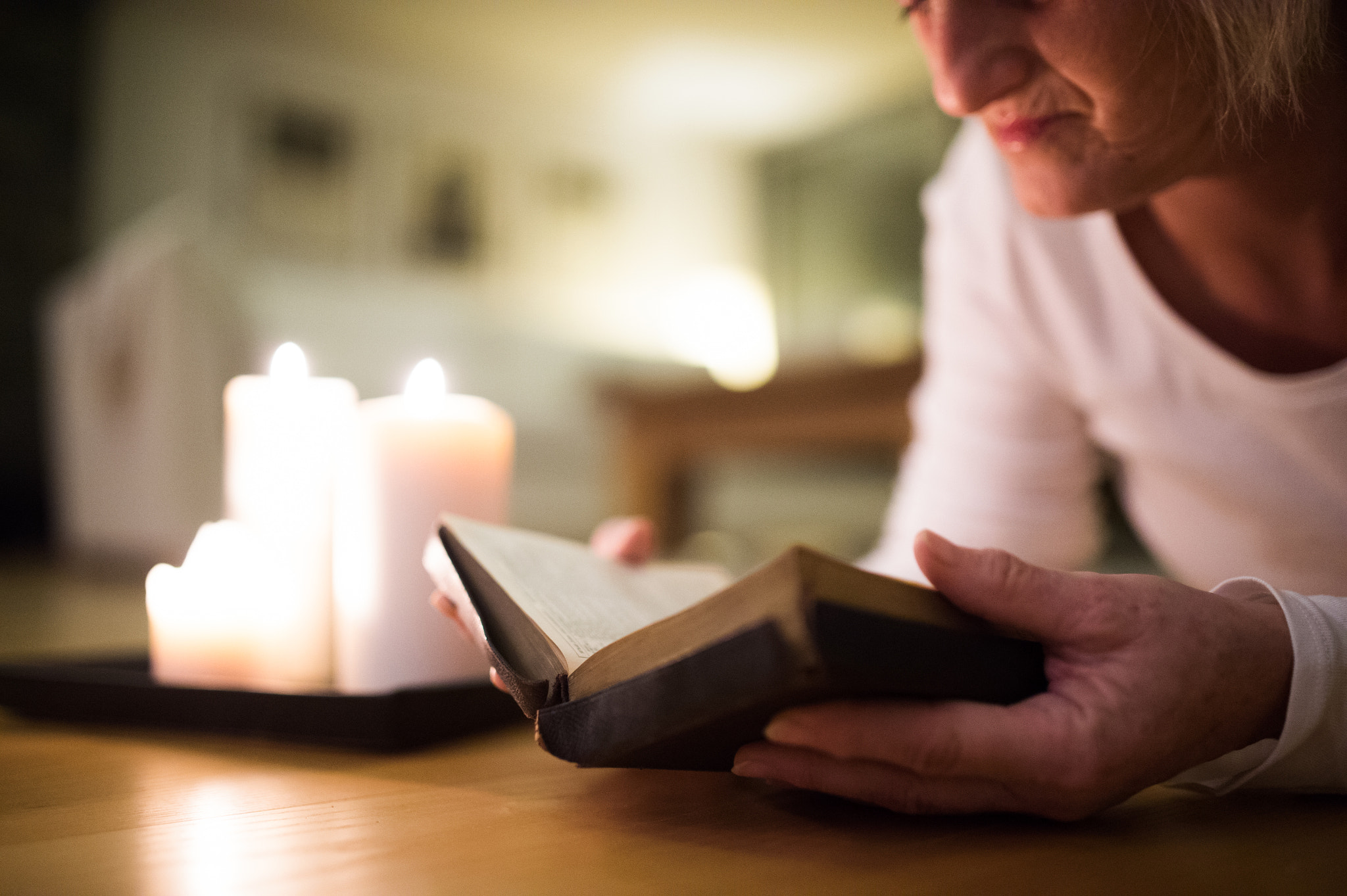 Nikon D4S + Sigma 35mm F1.4 DG HSM Art sample photo. Unrecognizable woman reading bible. burning candles next to her. photography