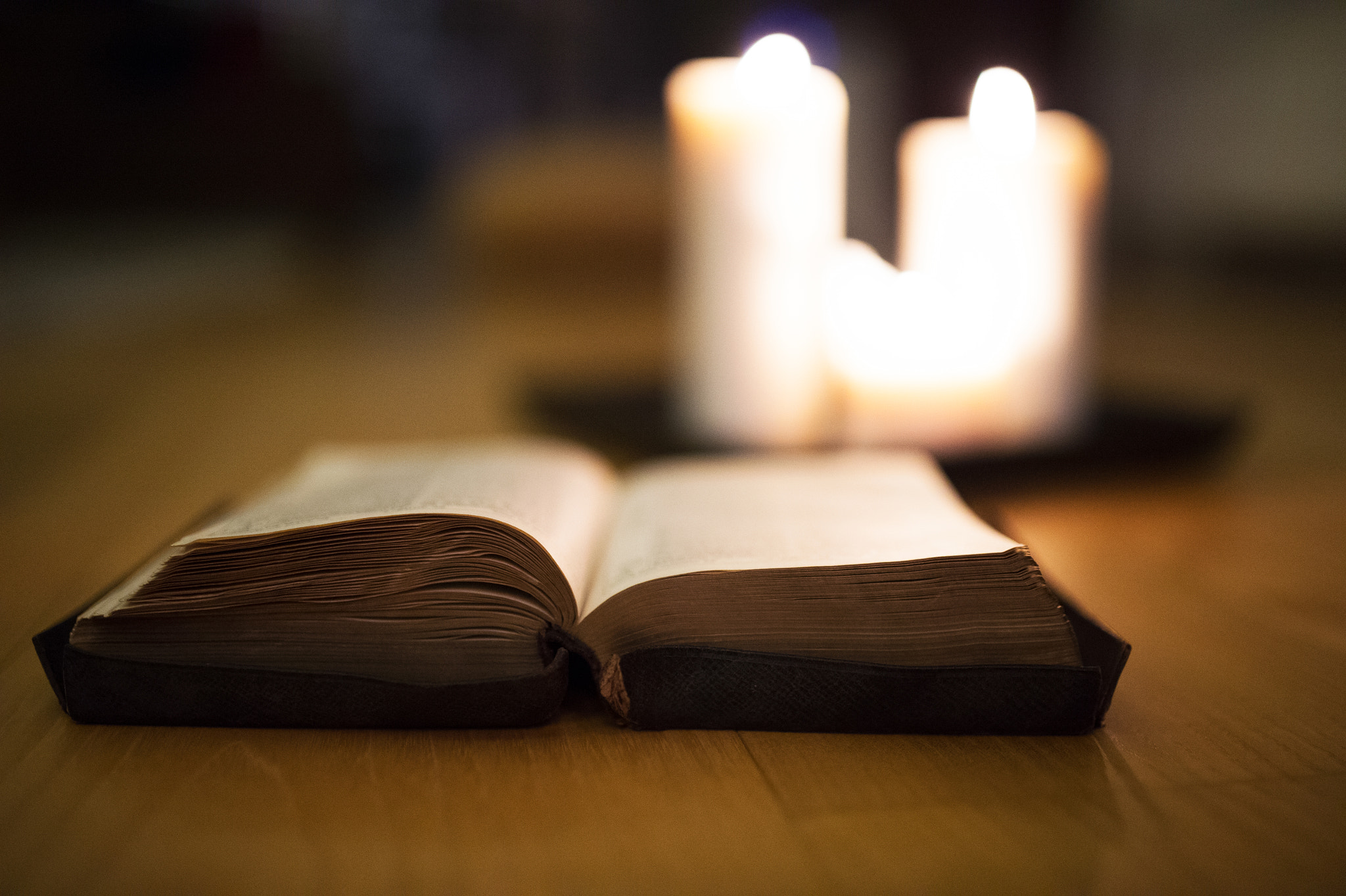 Nikon D4S sample photo. Bible laid on wooden floor, burning candles in the background photography