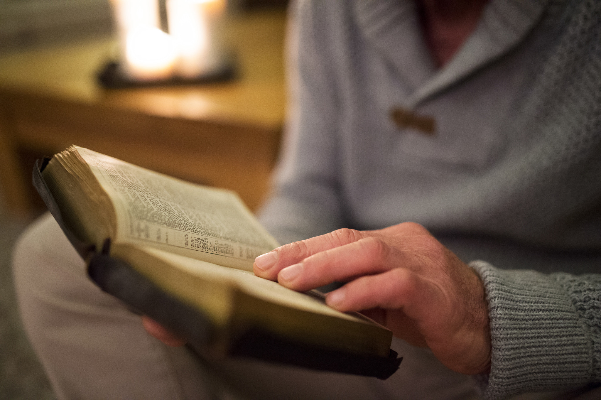 Nikon D4S + Sigma 35mm F1.4 DG HSM Art sample photo. Unrecognizable man at home reading bible, burning candles behind photography