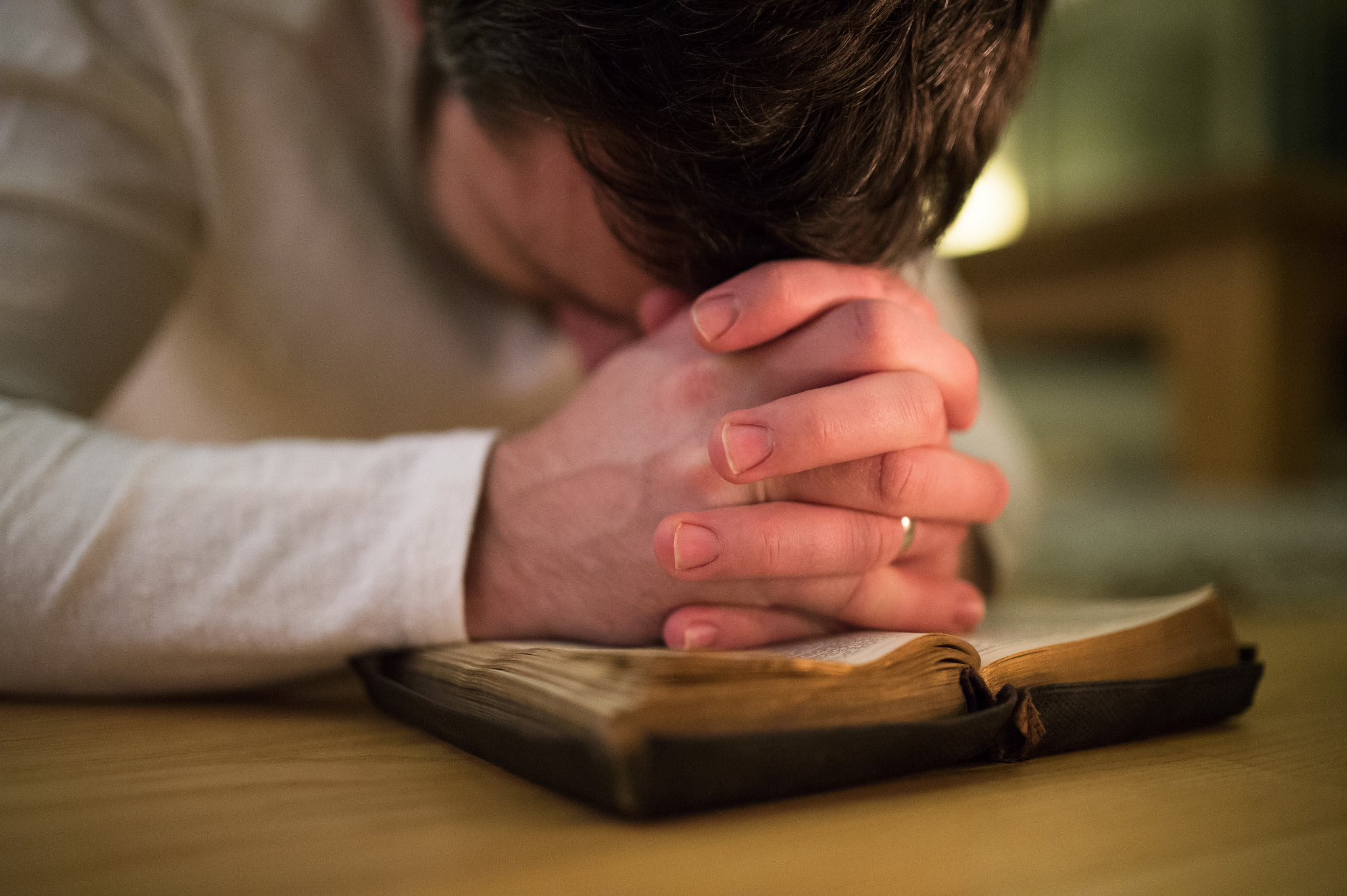 Nikon D4S sample photo. Unrecognizable man praying, kneeling on the floor, hands on bibl photography