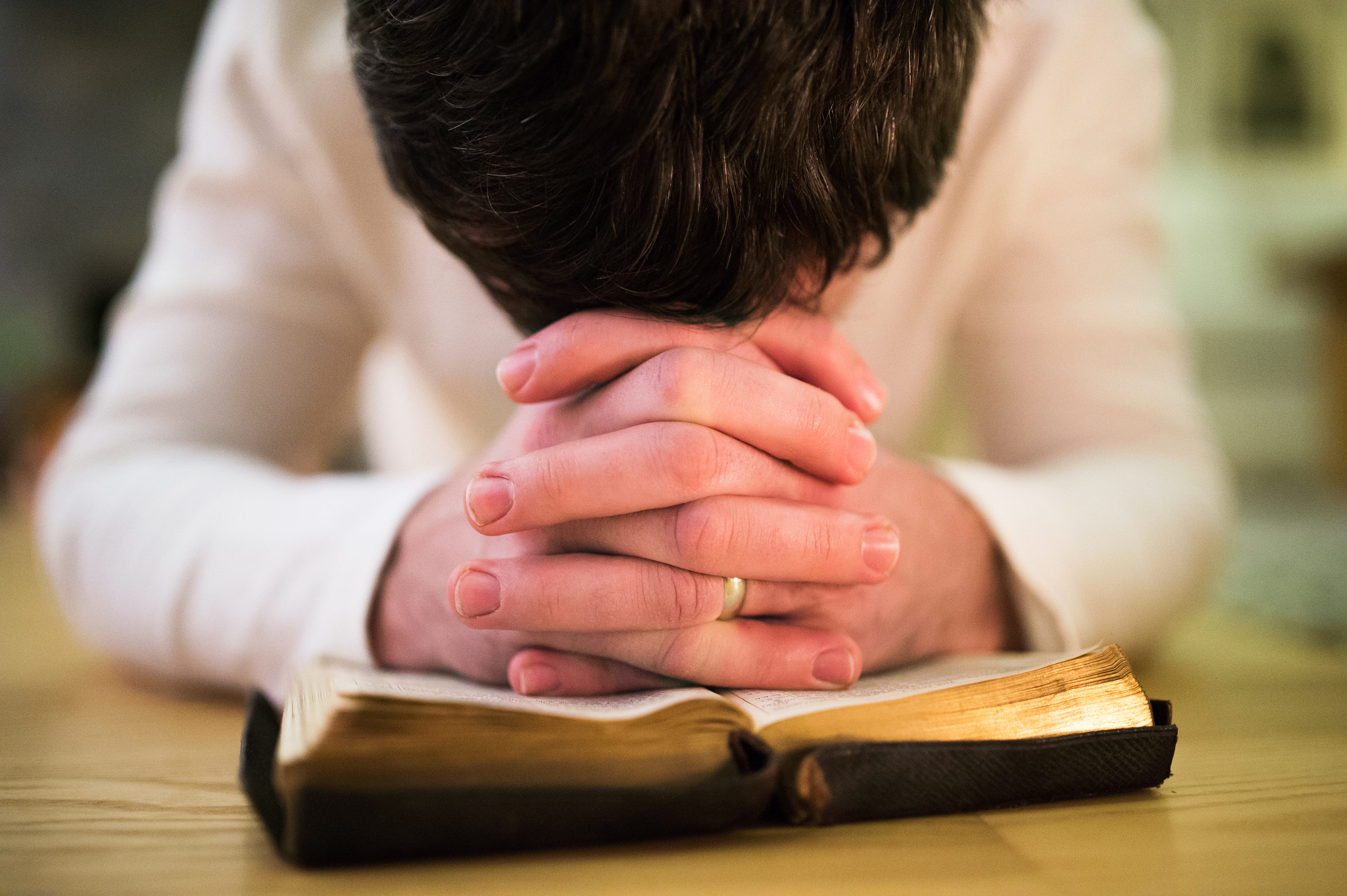 Nikon D4S sample photo. Unrecognizable man praying, kneeling on the floor, hands on bibl photography