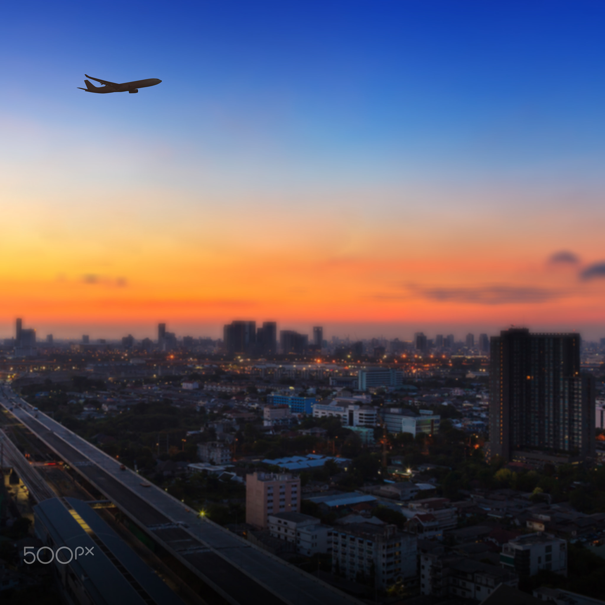 Silhouette of airplane flying in a sky over the city at sunrise