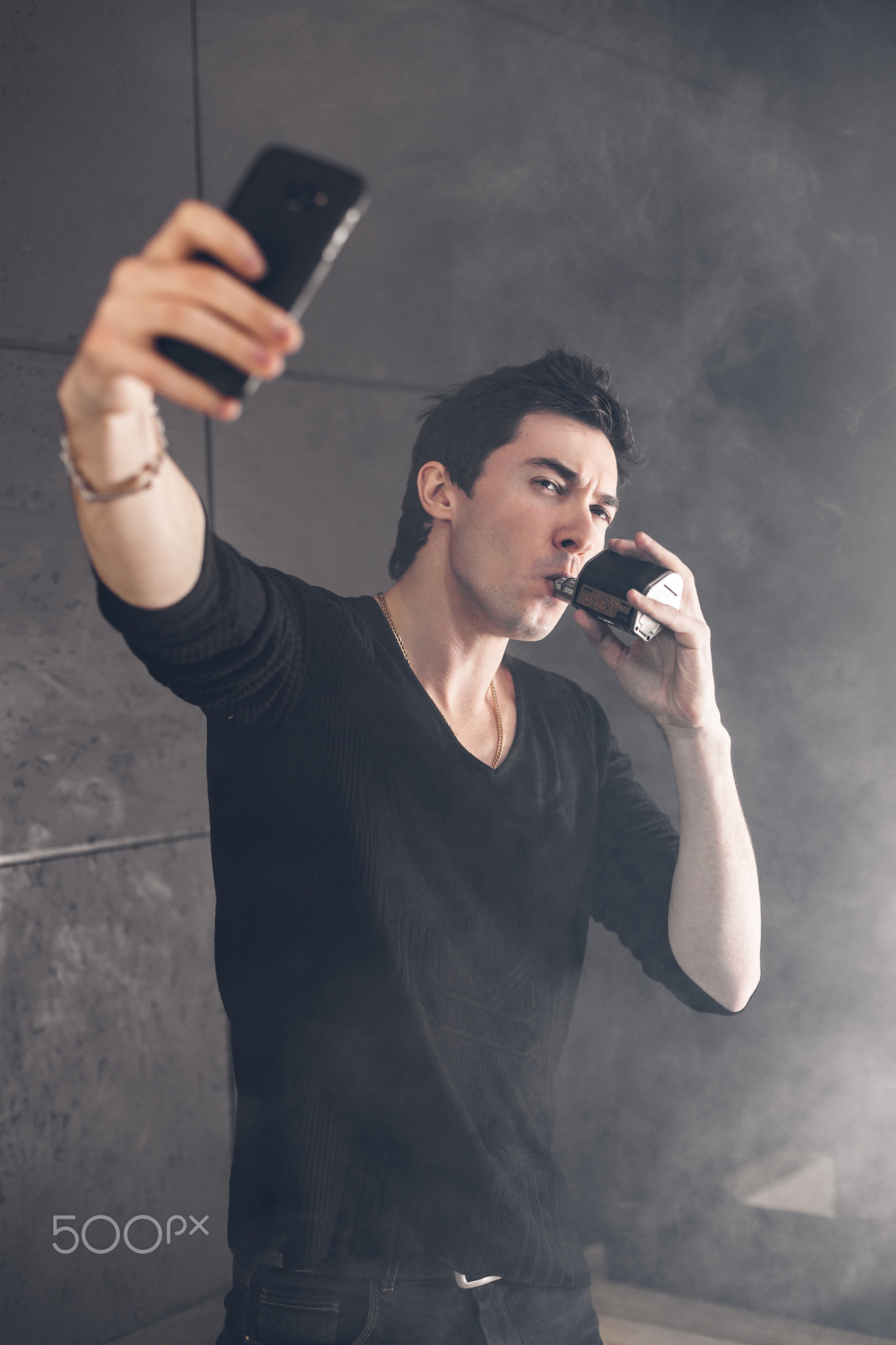 Vaping man holding a mod. A cloud of vapor. Black background.