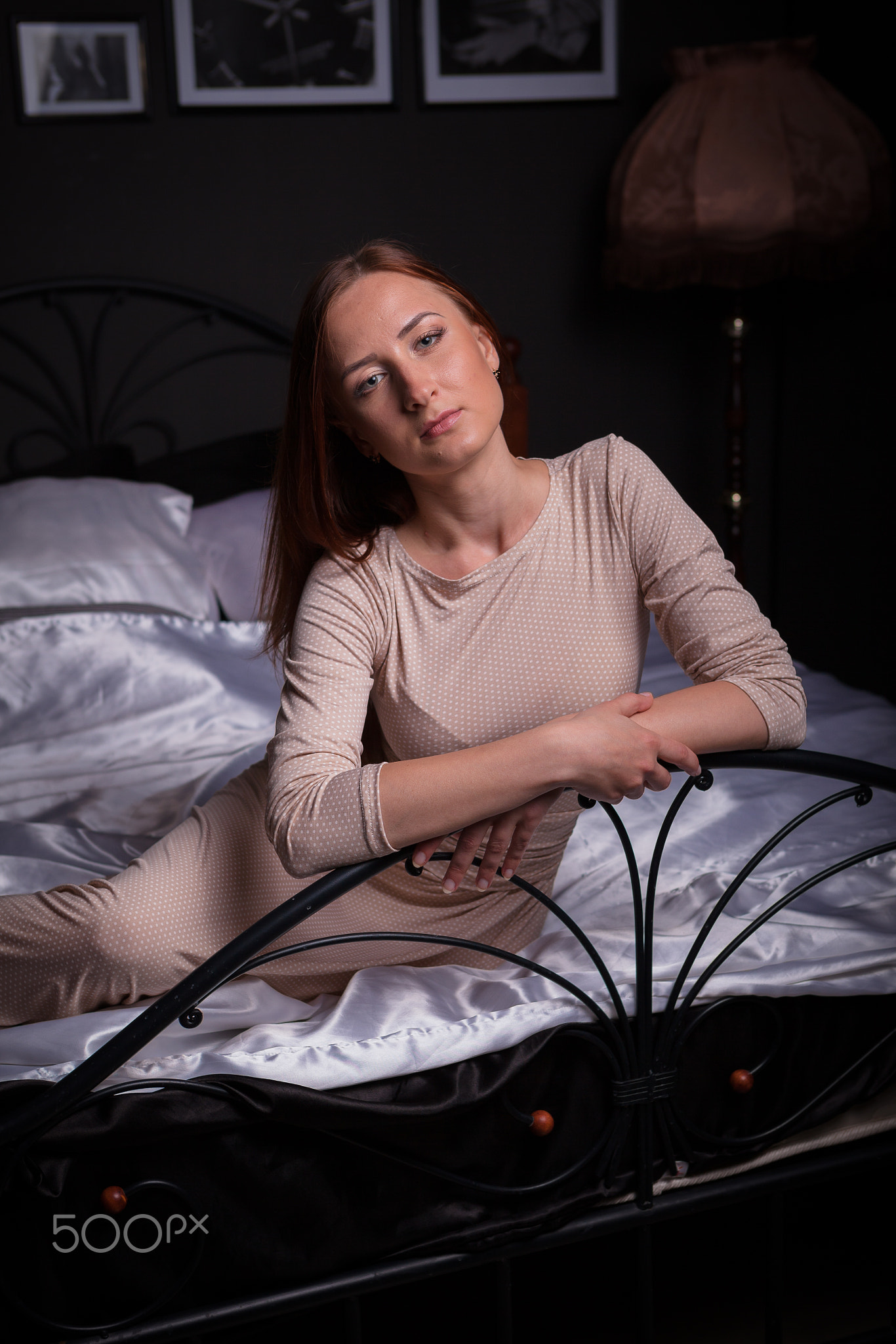 Beautiful young woman in stylish home interior, sitting on fairy bed, grey colored room