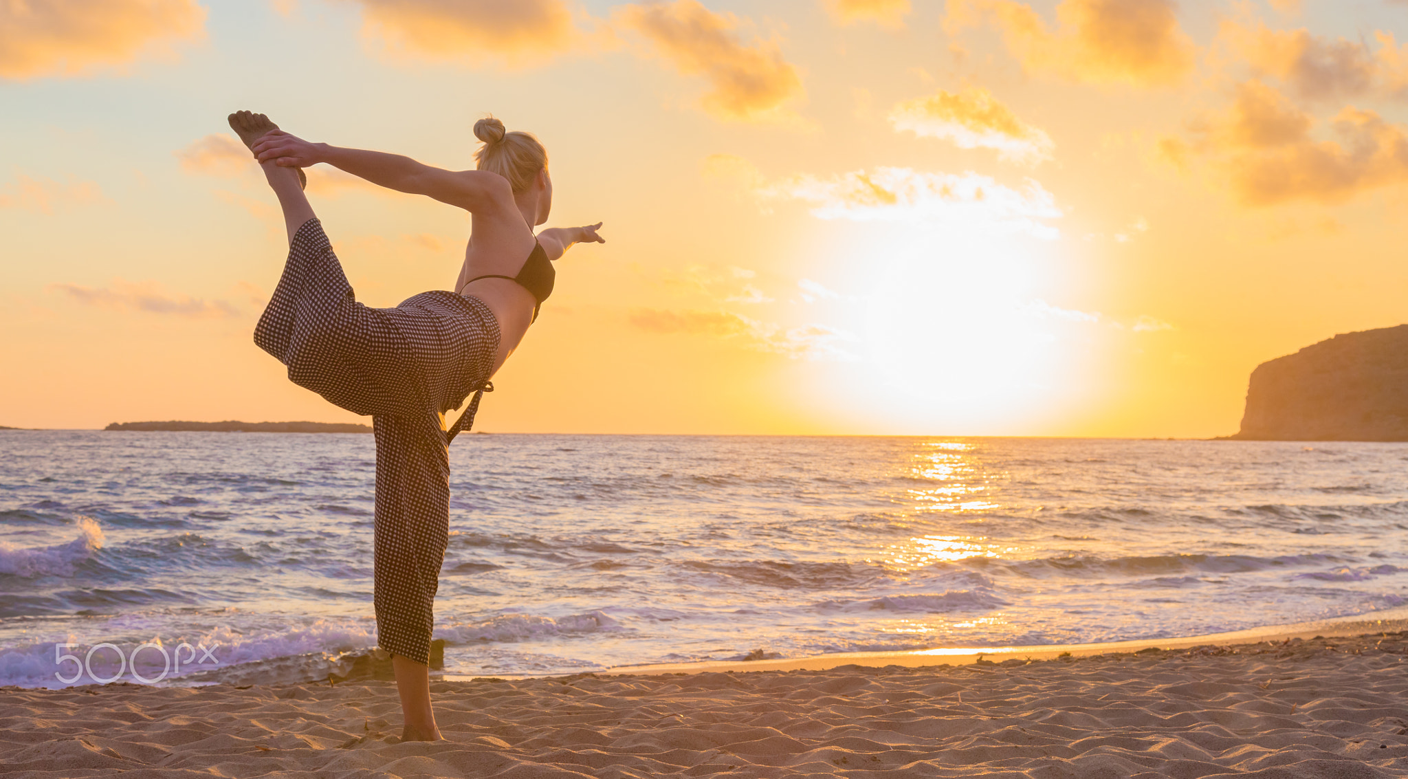 Woman practicing yoga on sea beach at sunset.