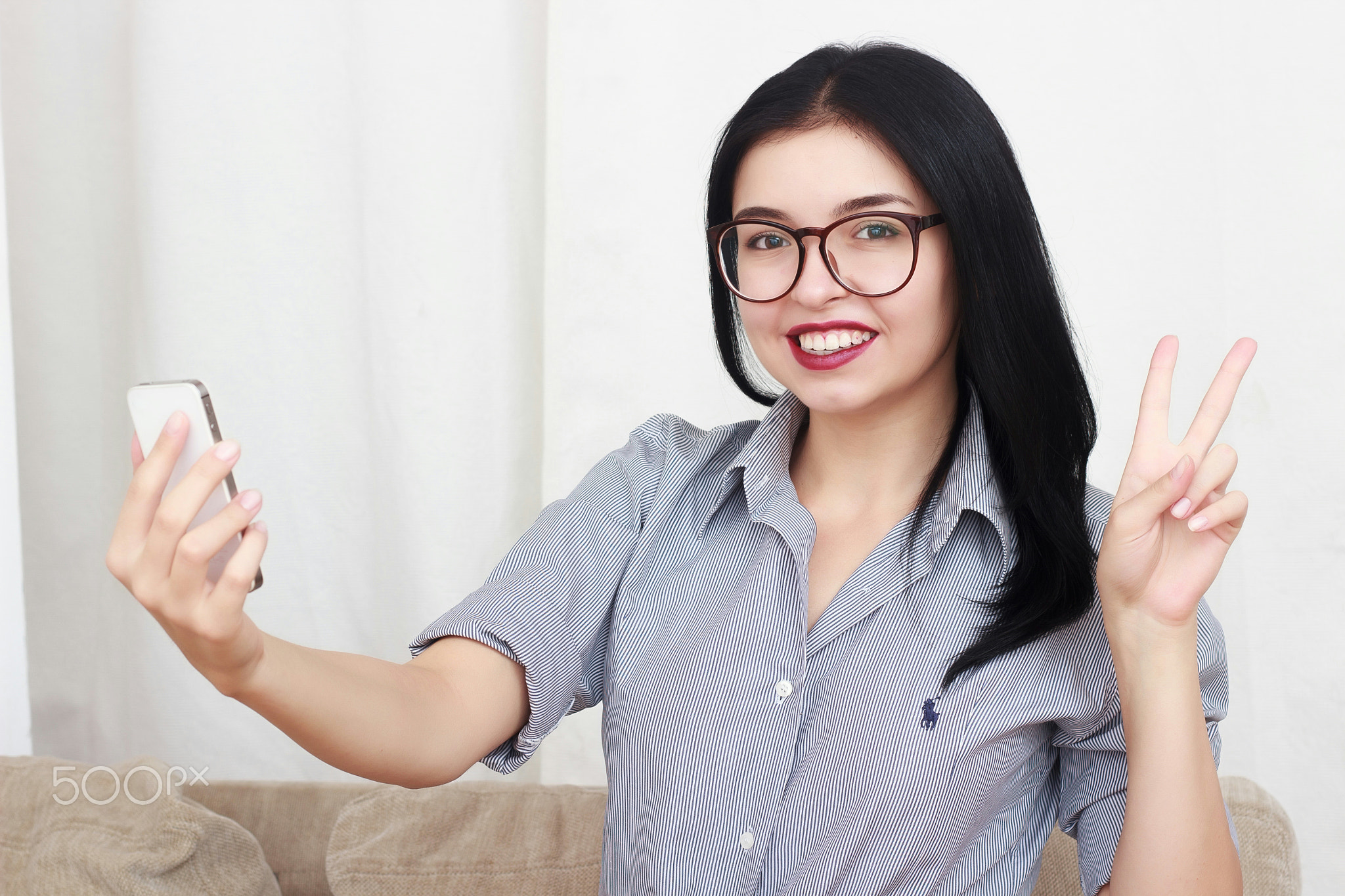 Beautiful woman wearing eyeglasses using a smart phone sitting on a sofa