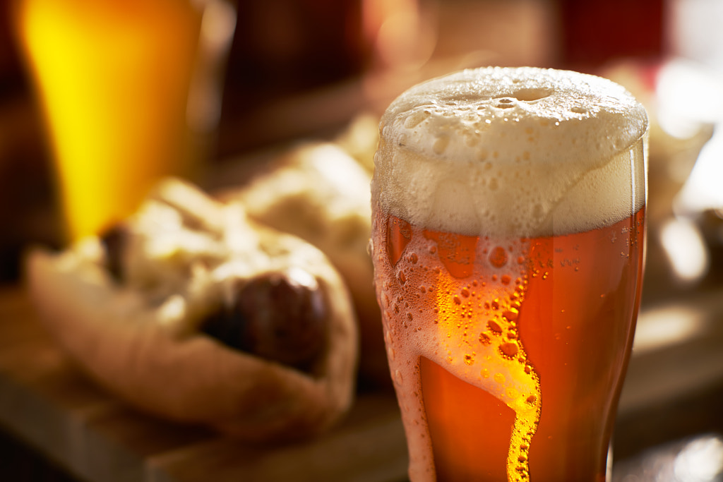 IPA beer with overflowing foamy head in mug served with bratwursts by Joshua Resnick on 500px.com