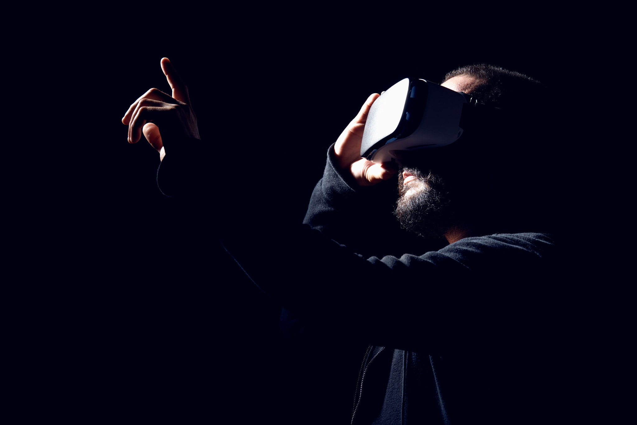 Young hipster bearded man wearing virtual reality goggles. Black background studio VR concept.