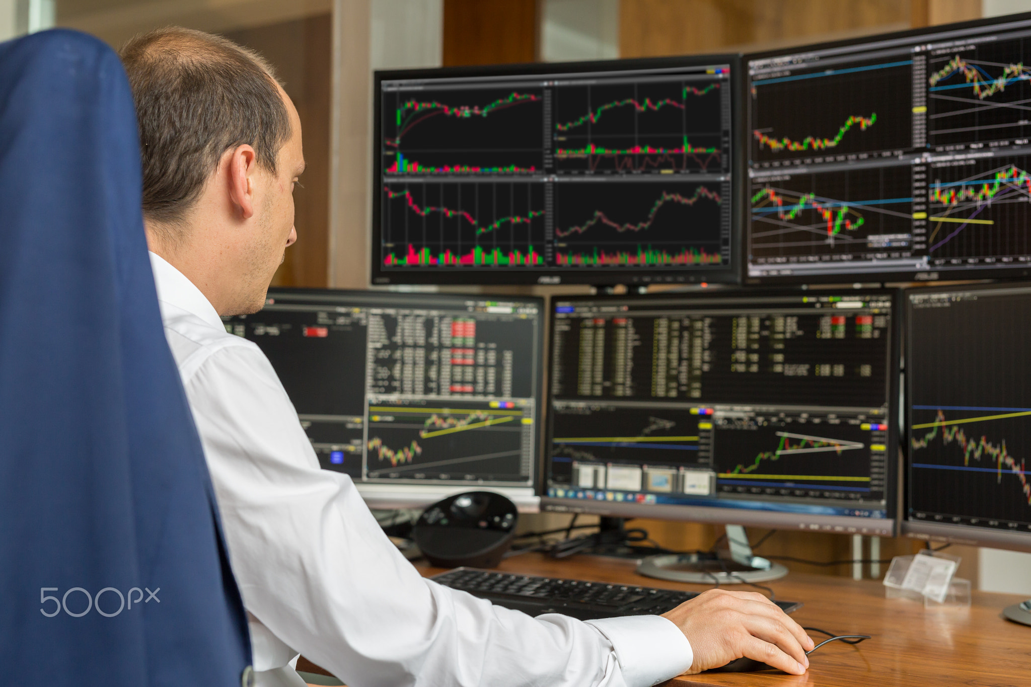 Rear view of stock trader analyzing data at multiple computer screens.