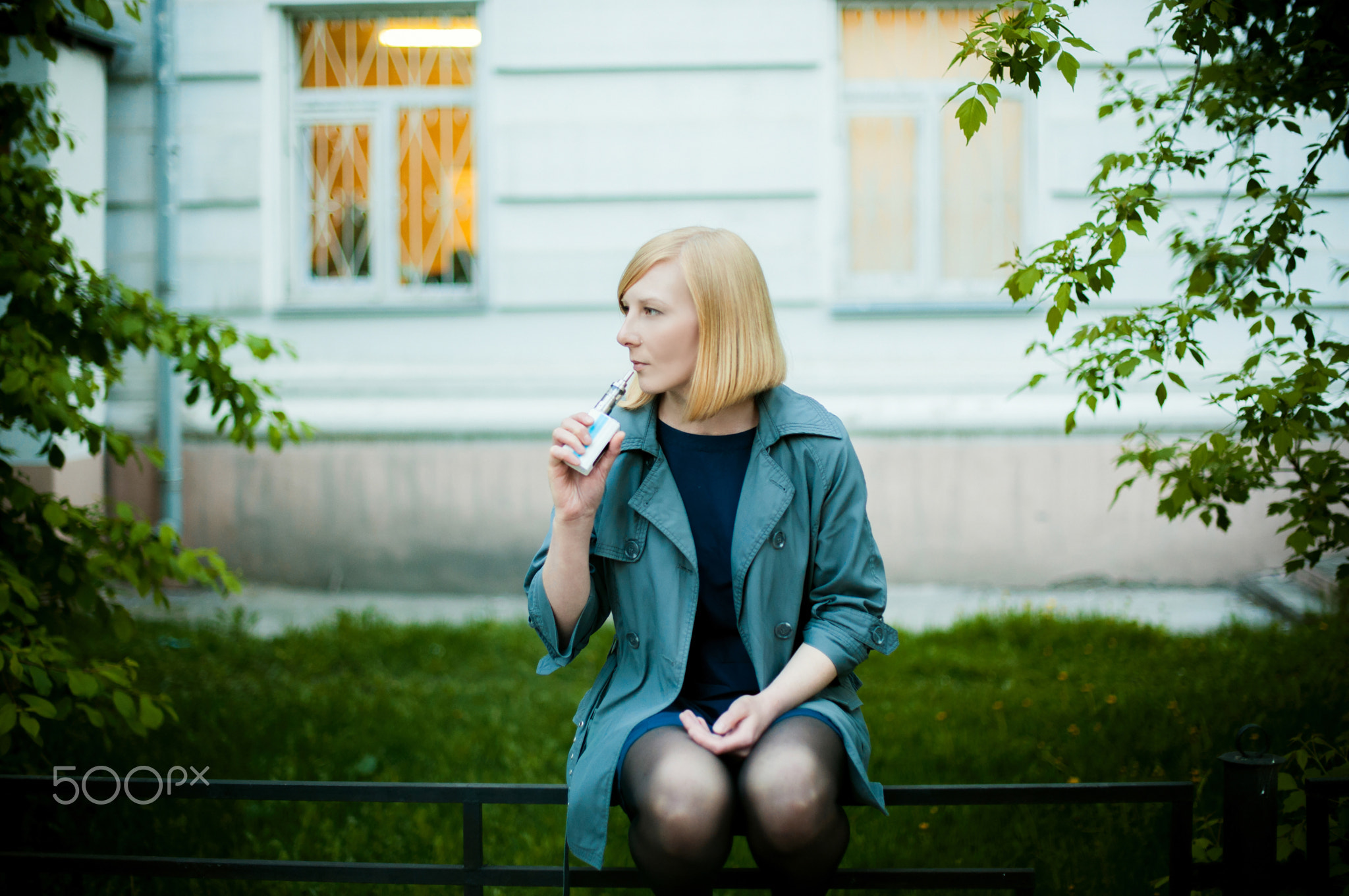 outdoor portrait of young blonde woman, wearing a raincoat, smoking electronic cigarette