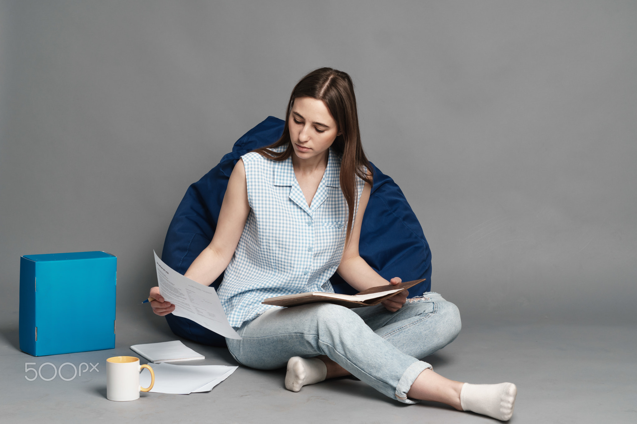 Woman sitting on a pillow bag and holding a notebook in hands. Isolated on gray background.