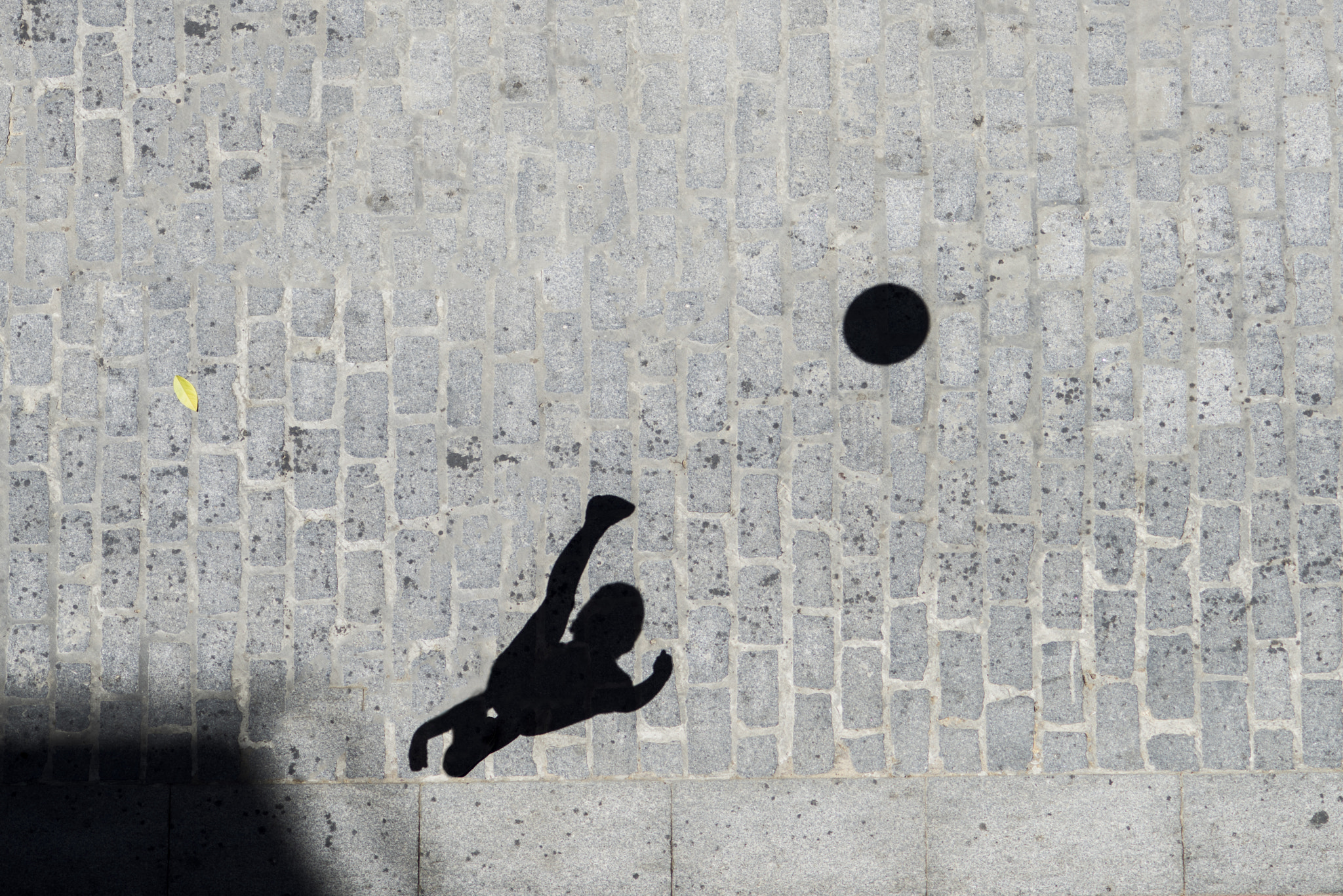 The shadow of a kid kicking a soccer ball