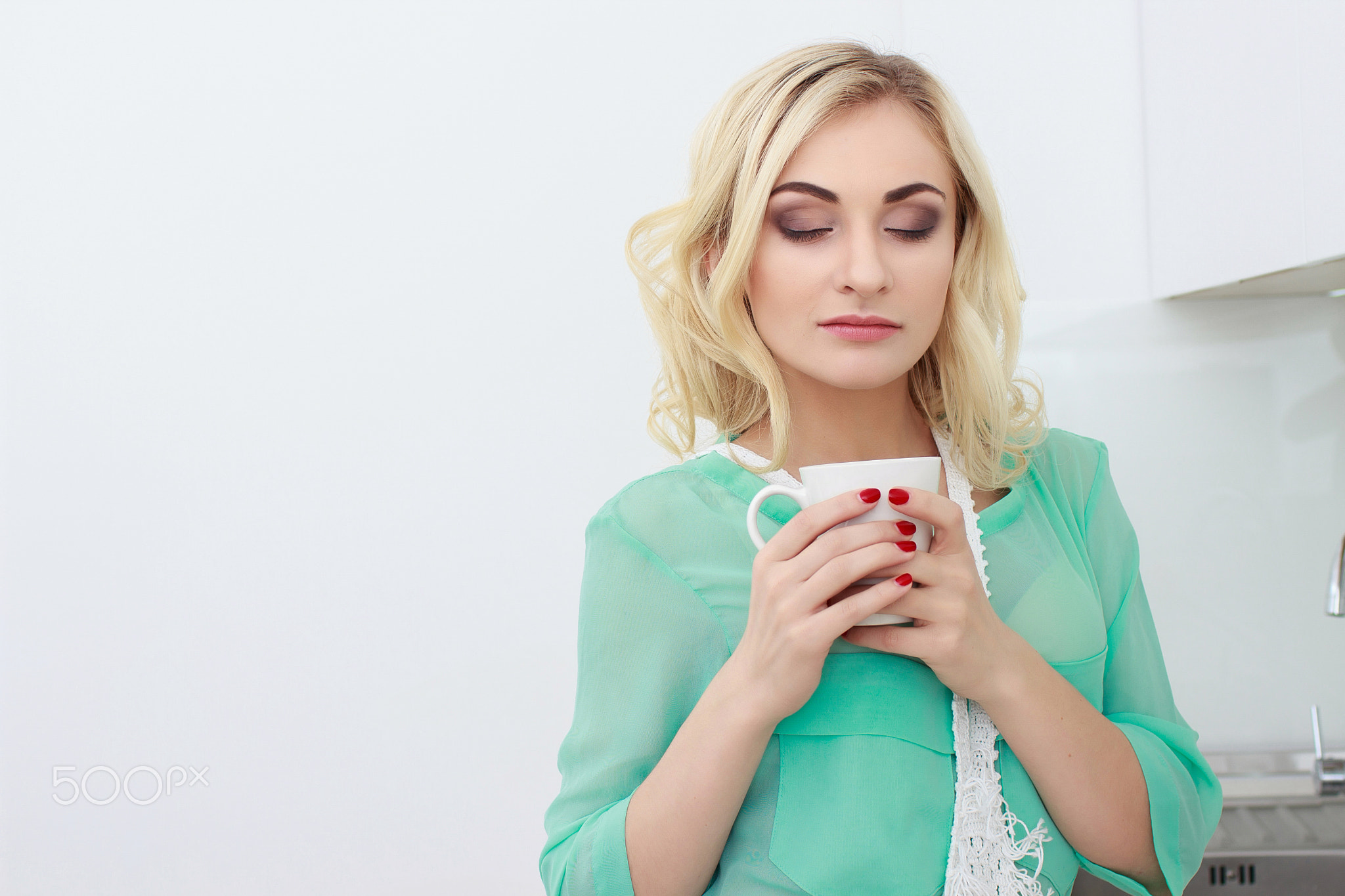 Happy woman holding a cup of coffee in her kitchen in the morning