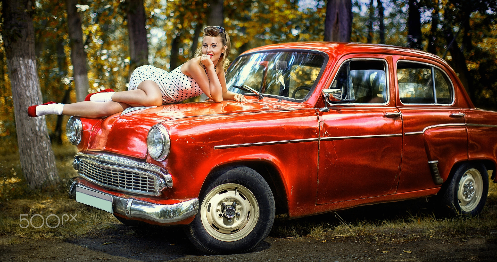 Pin-up girl in white dress on the hood of red retr