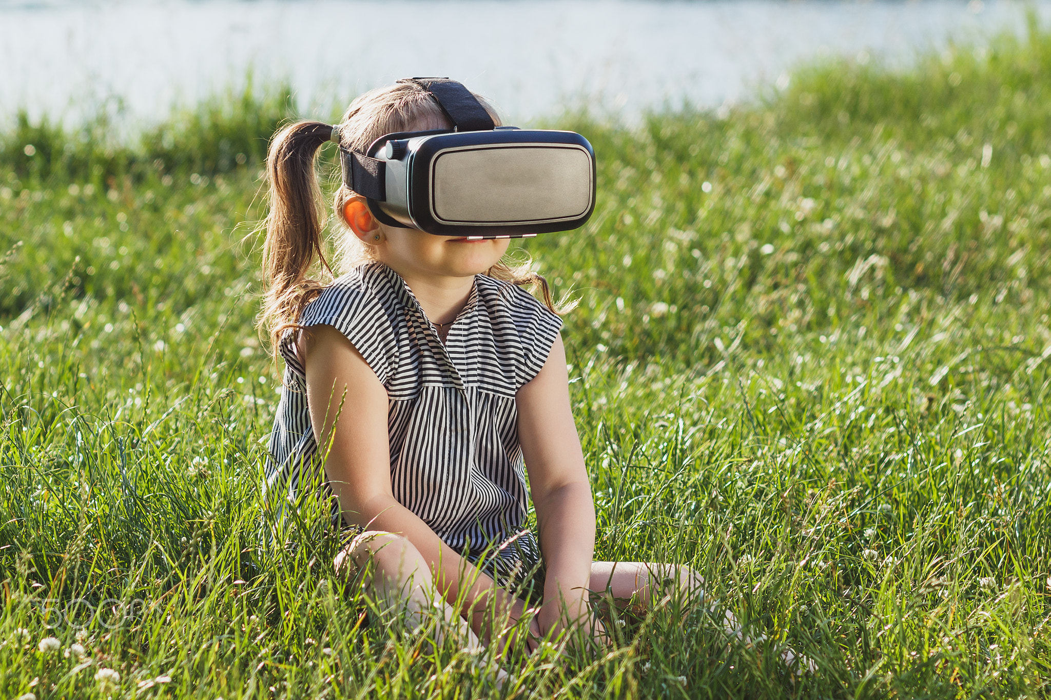 Little girl plays game with virtual reality glasses outdoors