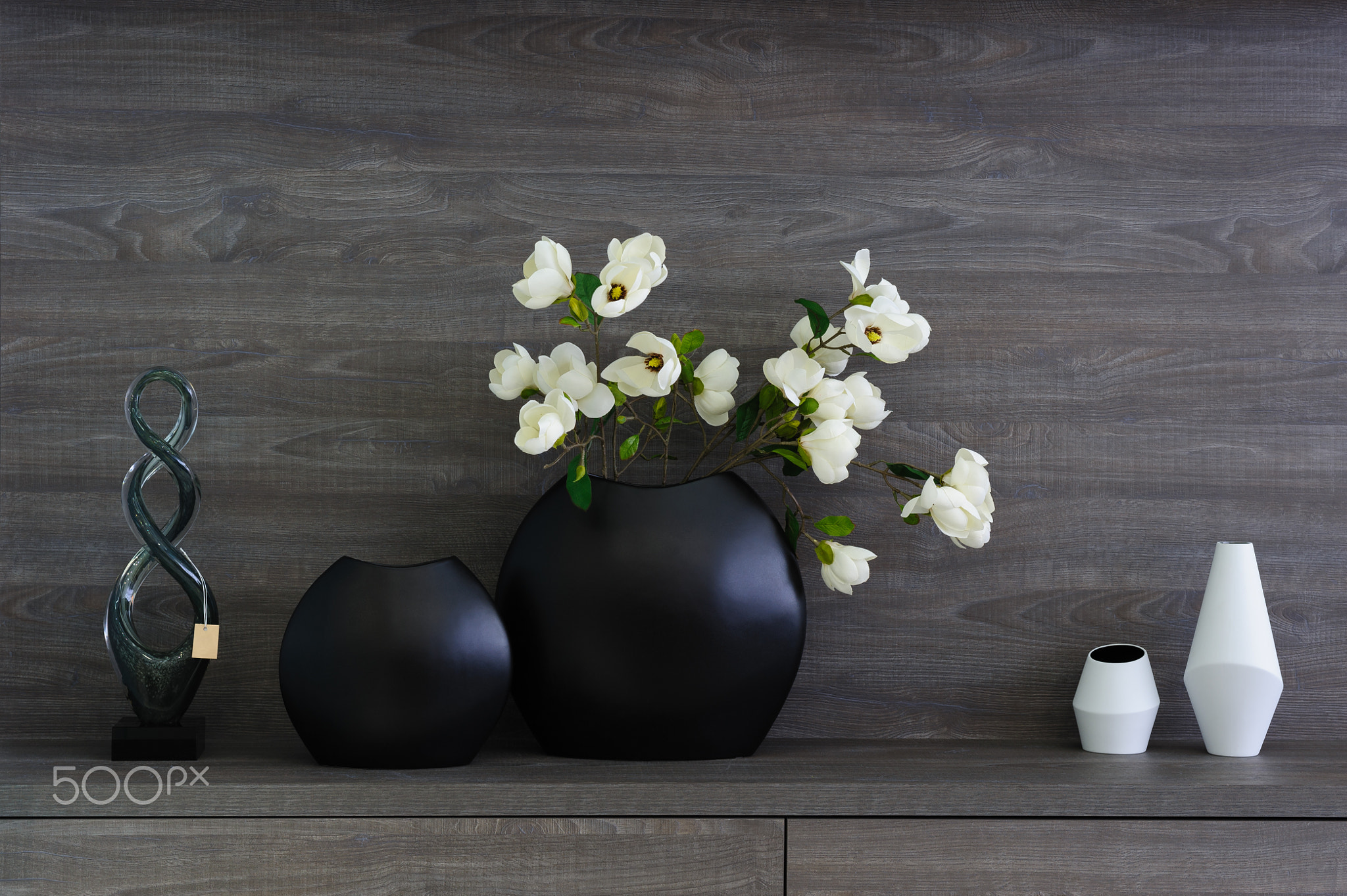 decorative vases and flowers at dark wooden shelf