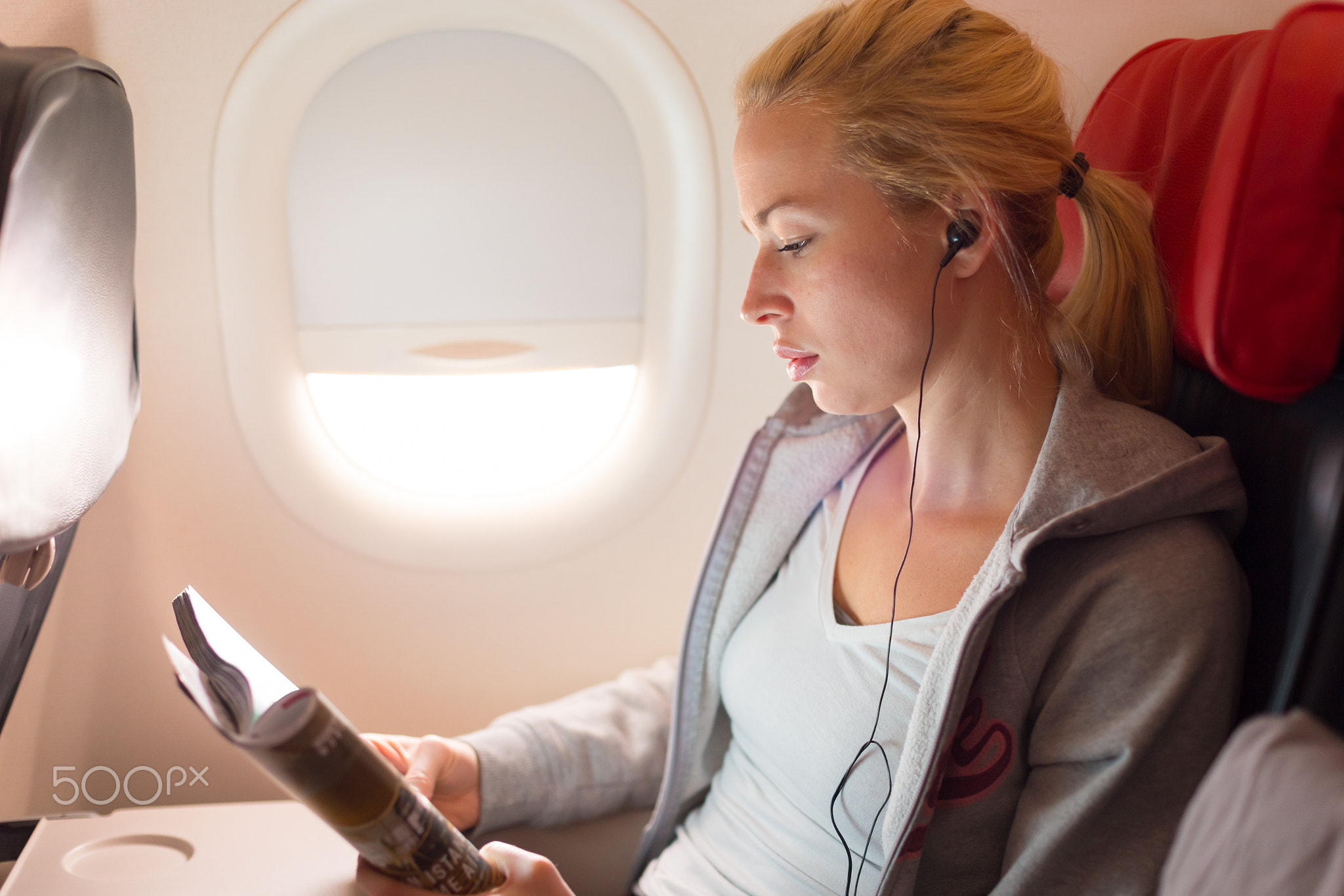 Woman reading magazine and listening to music on airplane.