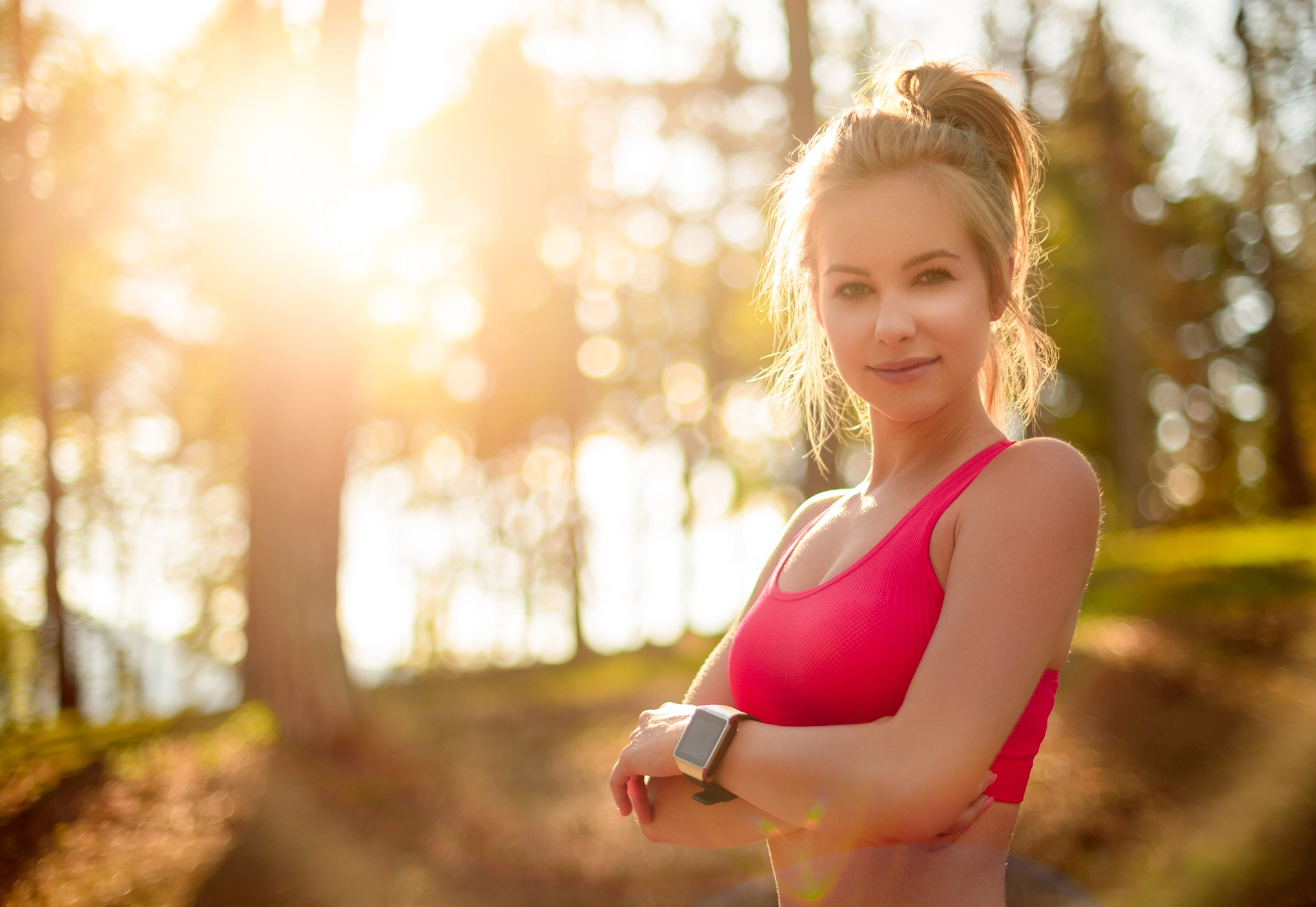 Attractive fit athletic woman in a forest, wearing smart watch, taking a break from intense...