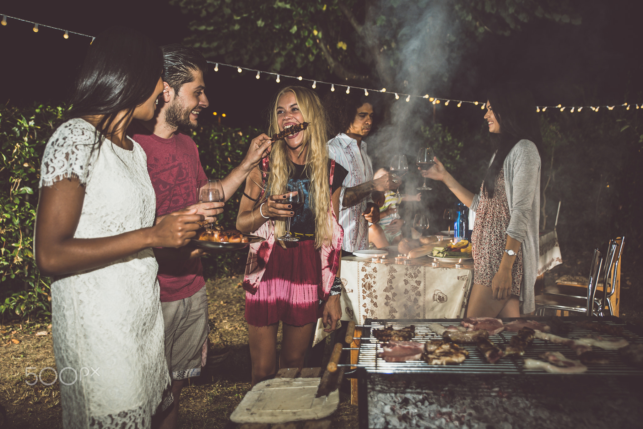 Group of friends making barbecue in the backyard at dinner time