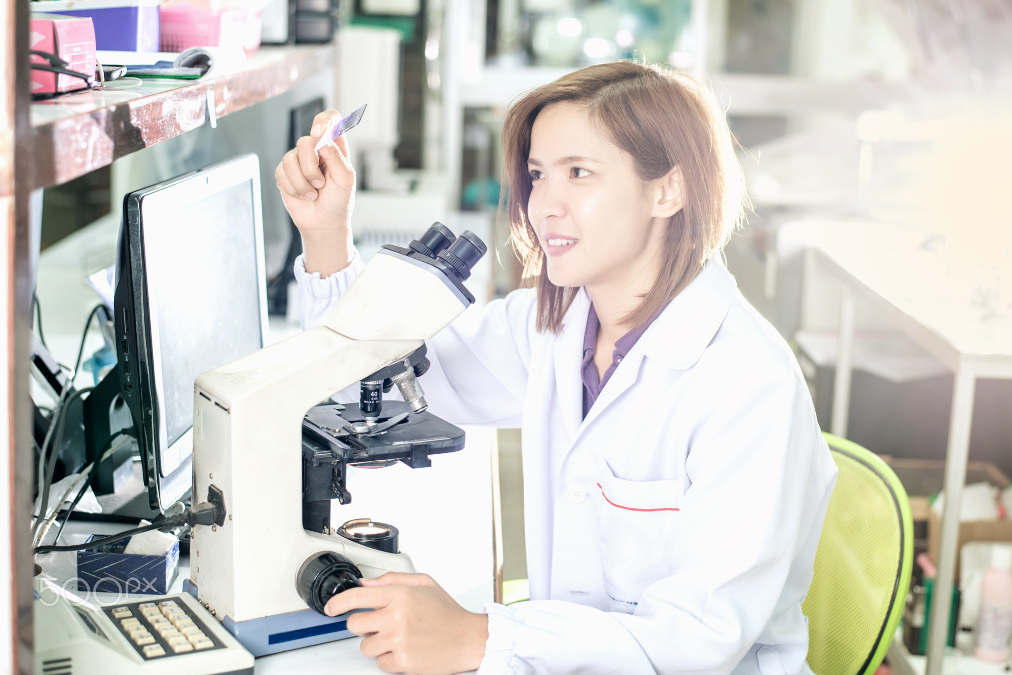 Portrait of a female researcher working in a lab scientist using microscope with colleague...