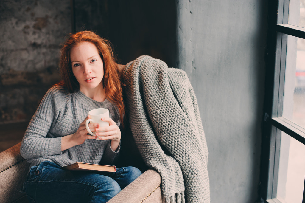 happy redhead woman relaxing at home in cozy winter or autumn weekend with book and cup of hot... by Maria Kovalevskaya on 500px.com