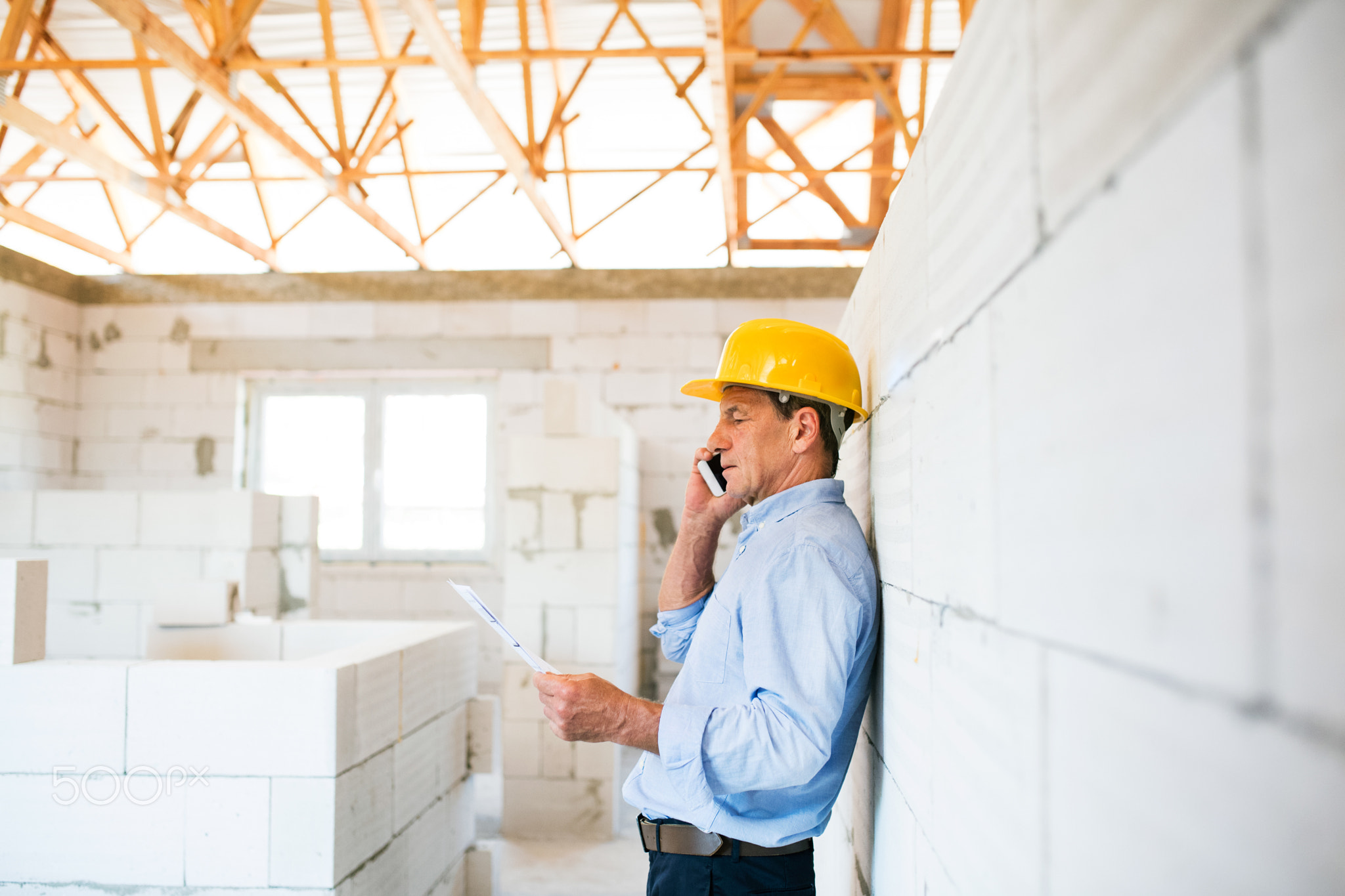 Senior architect with smartphone at the construction site.