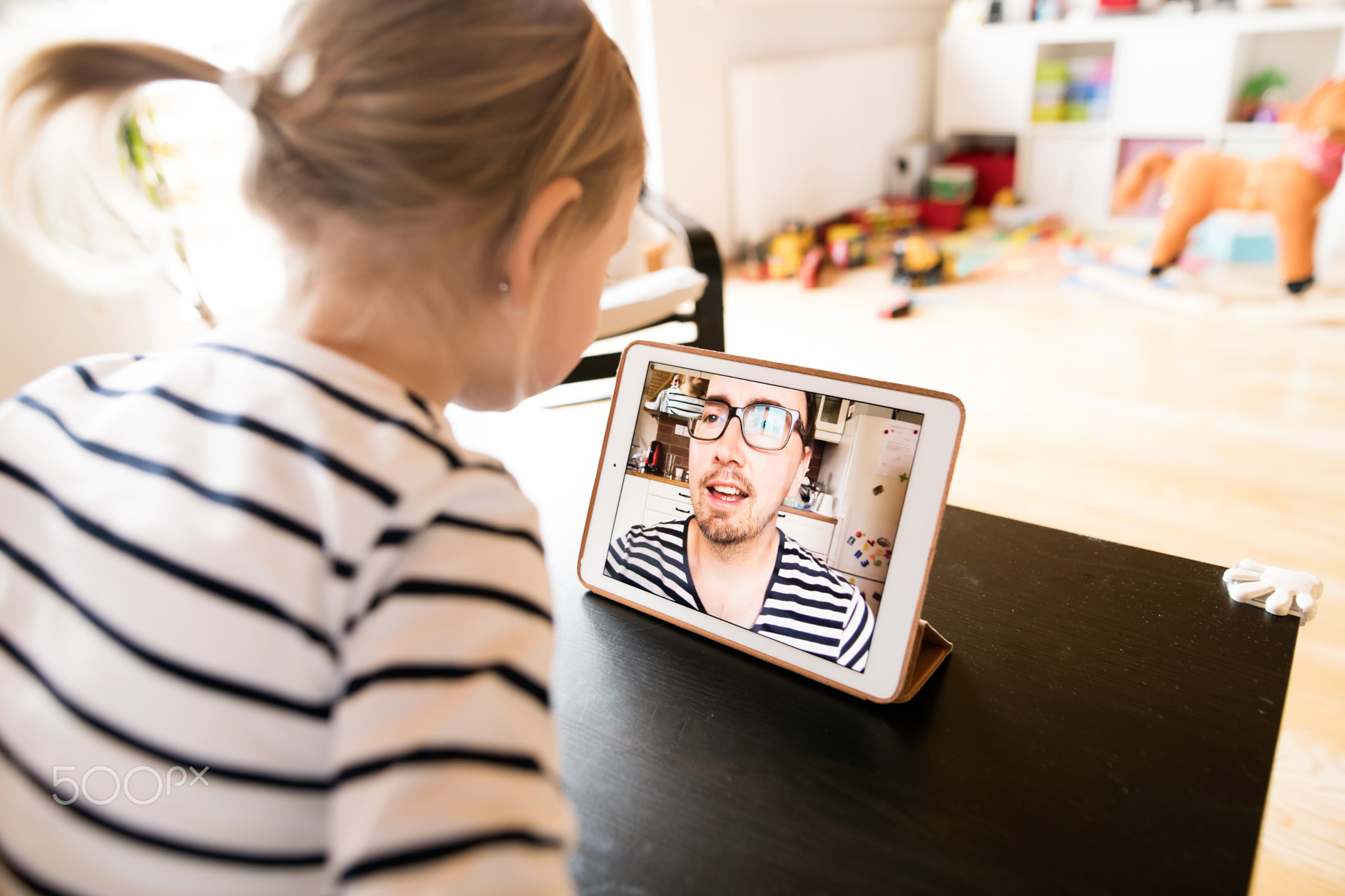 Little girl at home with tablet, video chatting with her father.