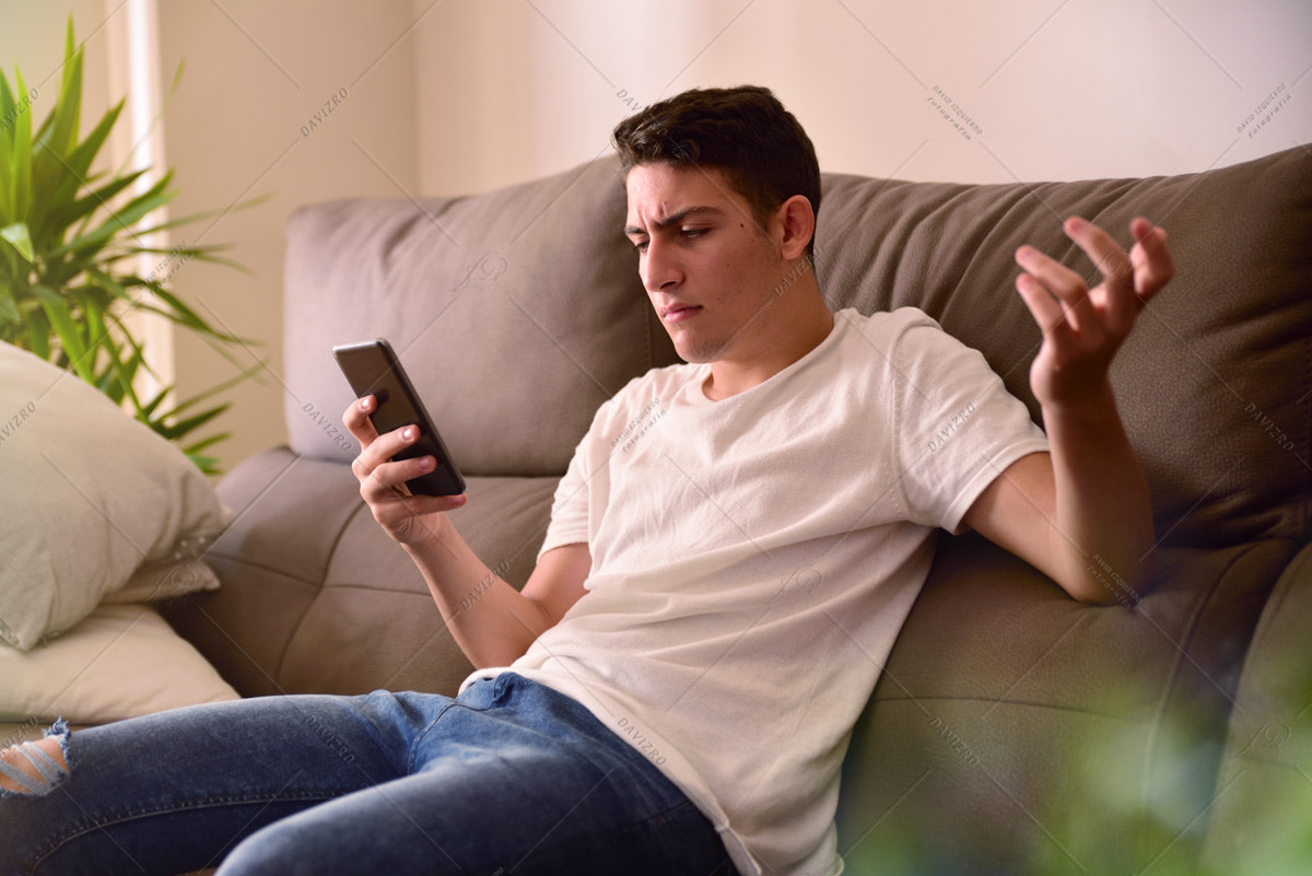 Teenager in disagreement with news on smartphone on sofa