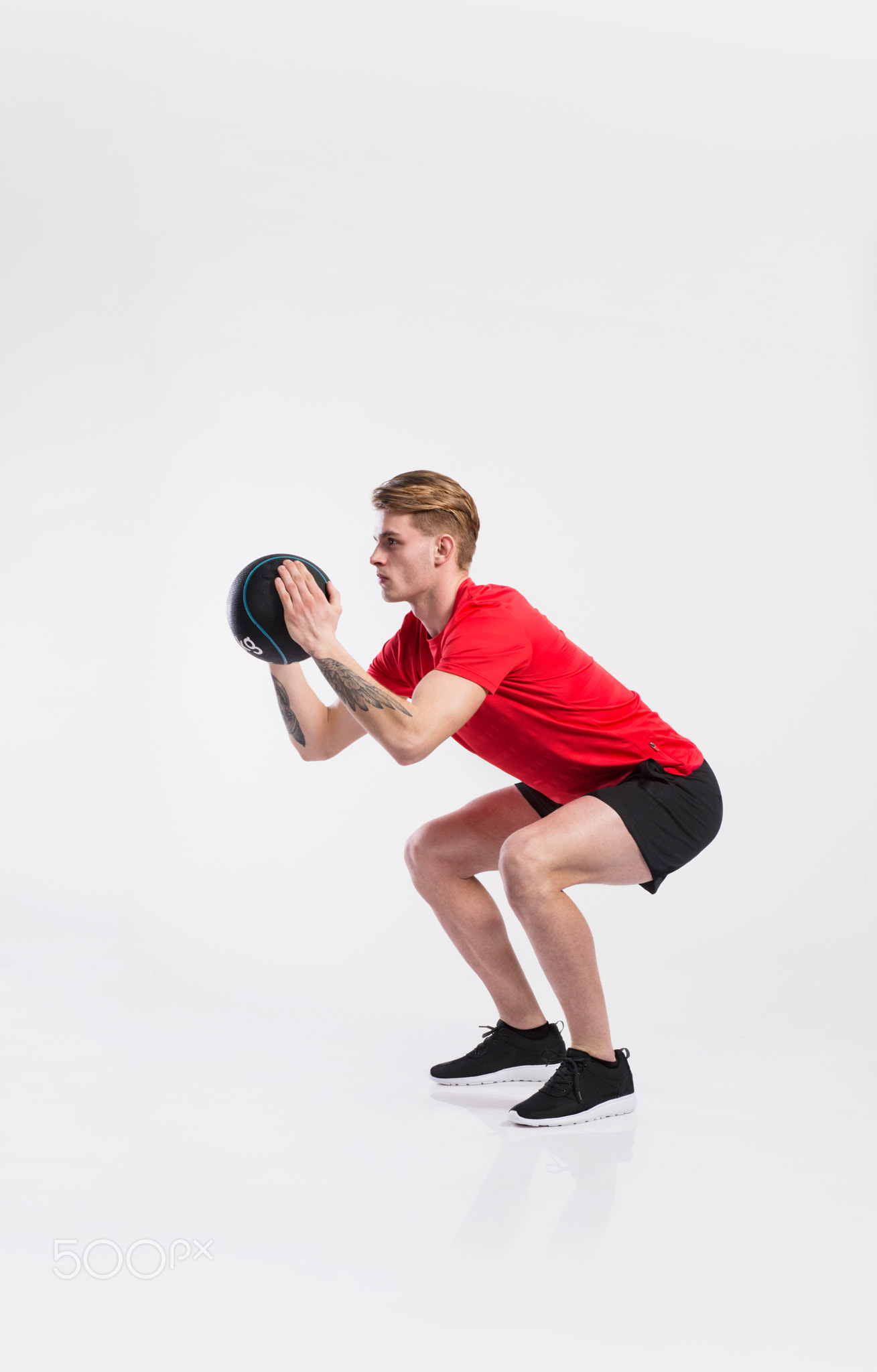 Fitness man holding medicine ball, doing squat, studio shot.