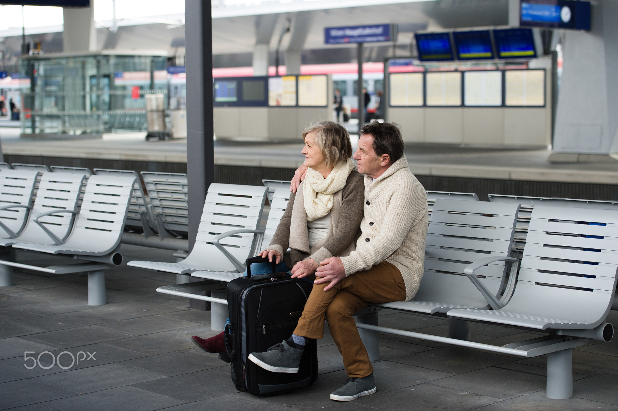 Senior couple waiting on train station, looking at watch.