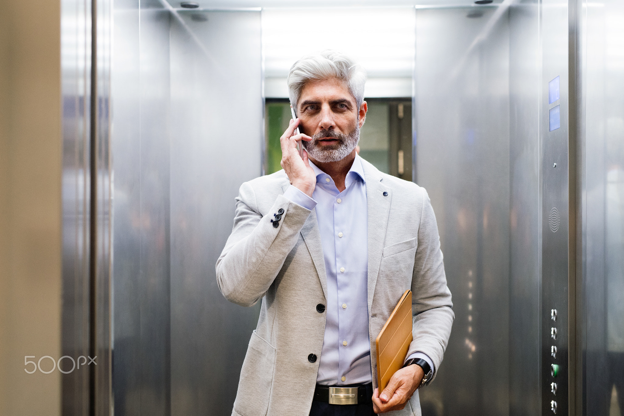 Mature businessman with smartphone in the elevator.