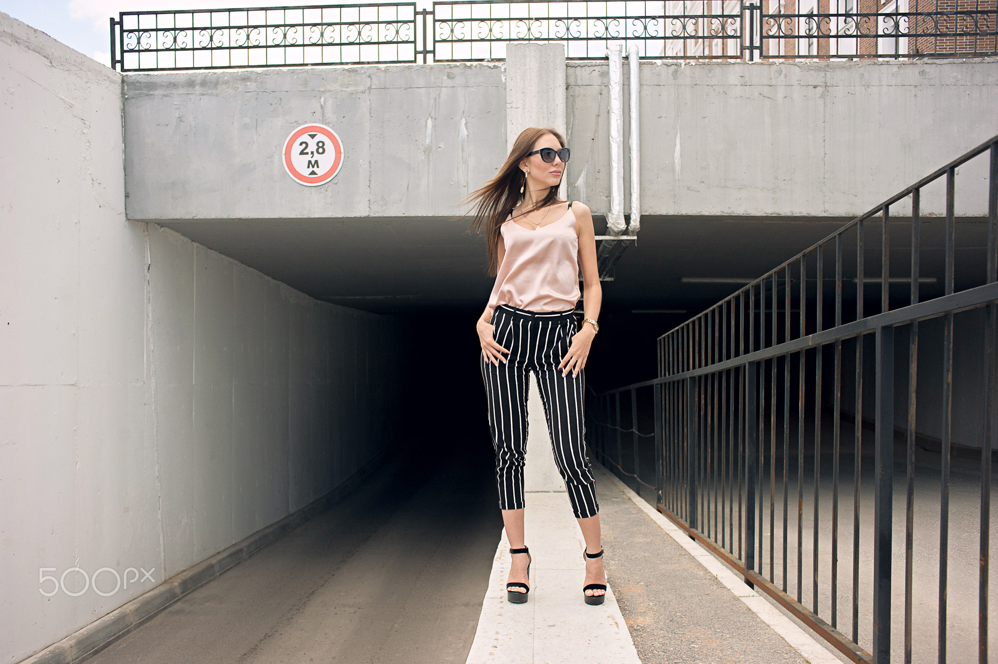 Beautiful young woman standing at the entrance to the underground garage. The model wears stylish...