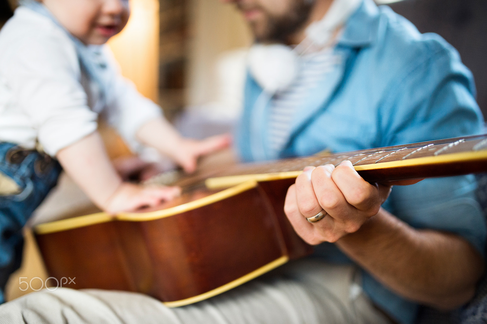 Little boy at home playing guitar with his father.