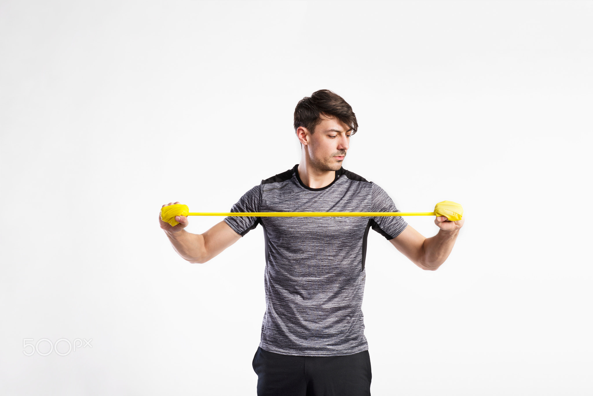 Handsome fitness man working out with rubber band, studio shot.