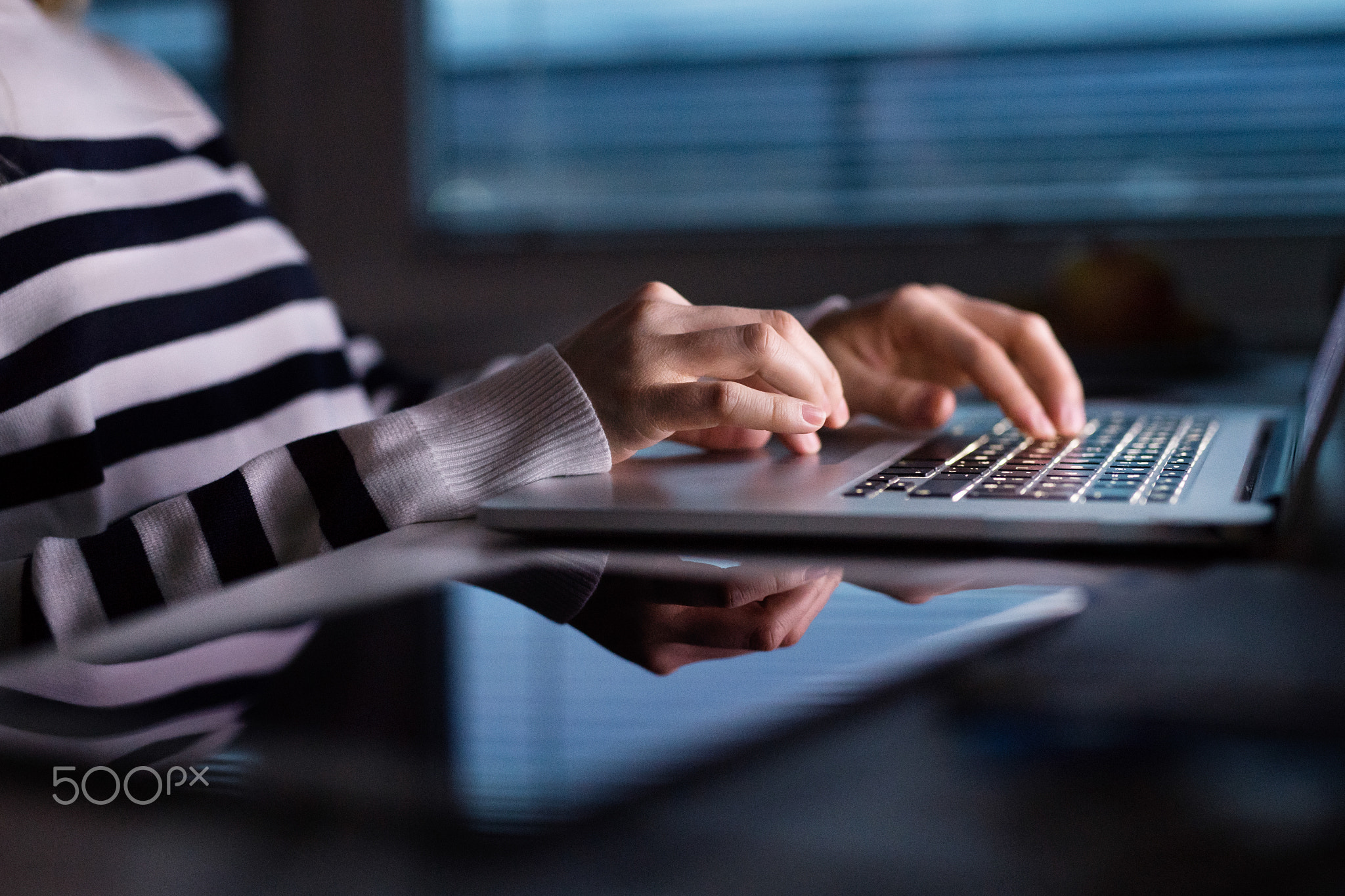 Unrecognizable woman sitting at desk working on laptop.