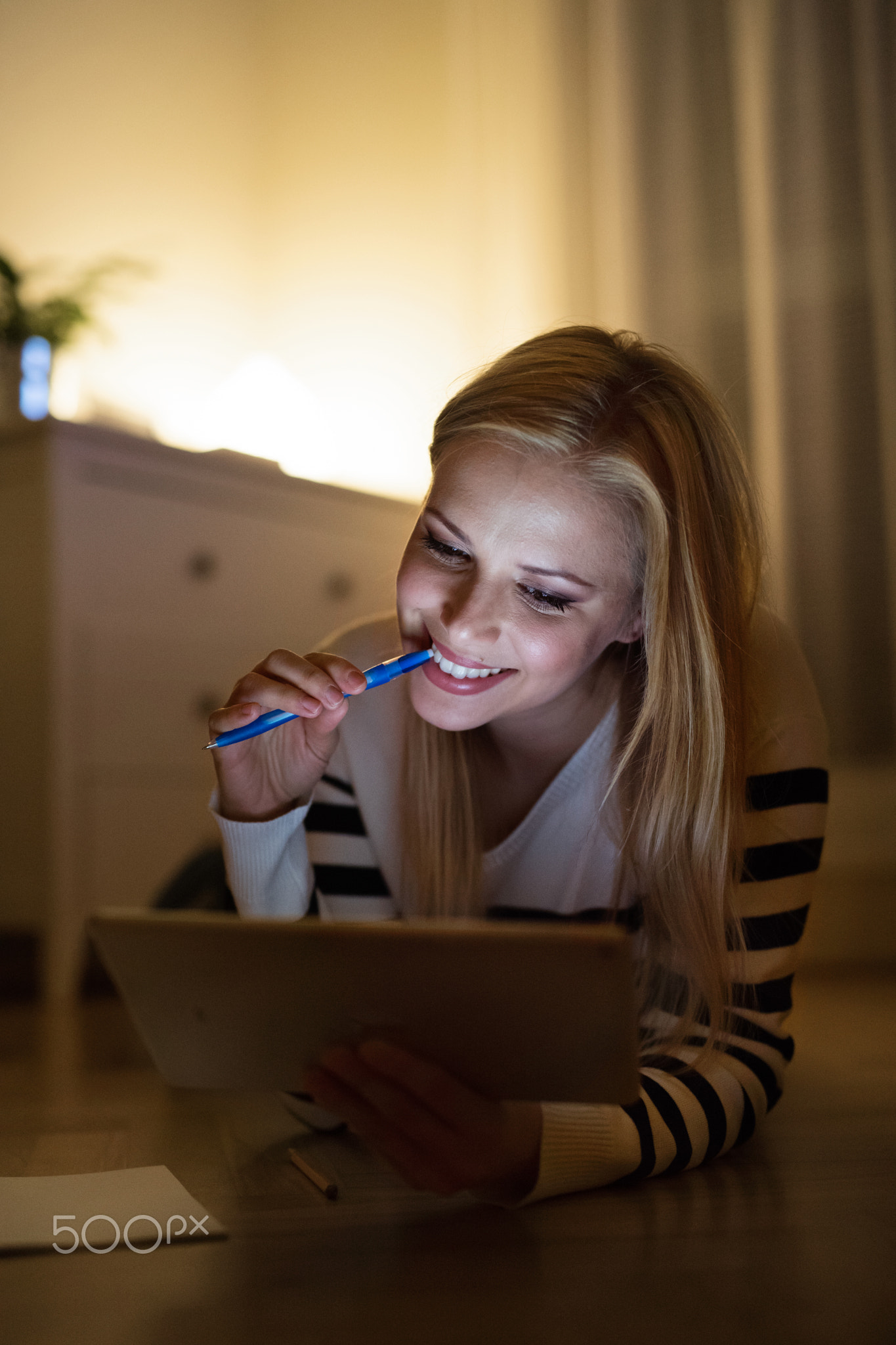 Woman lying on the floor, working on tablet at night.