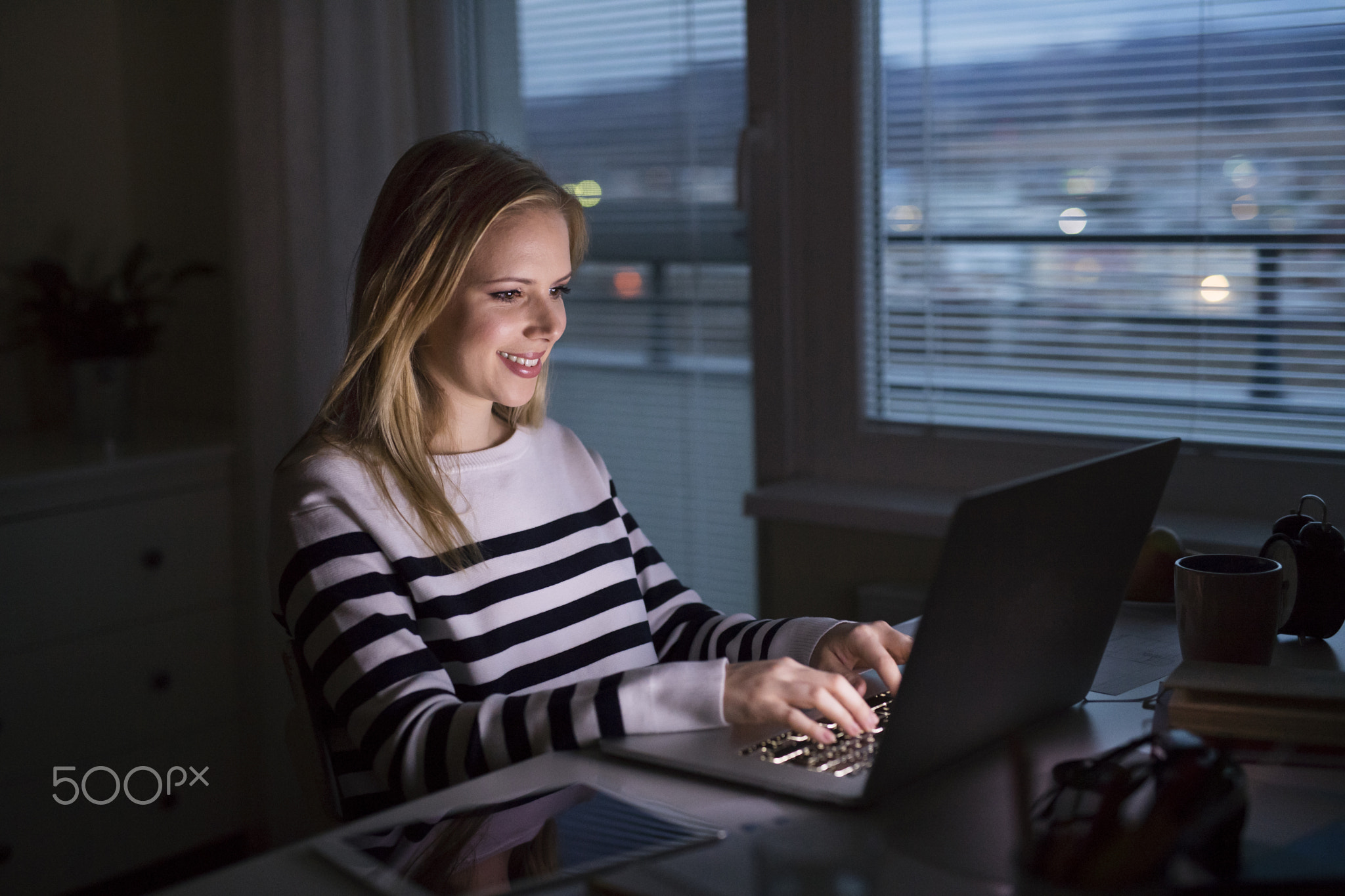 Woman sitting at desk and working on laptop at night.