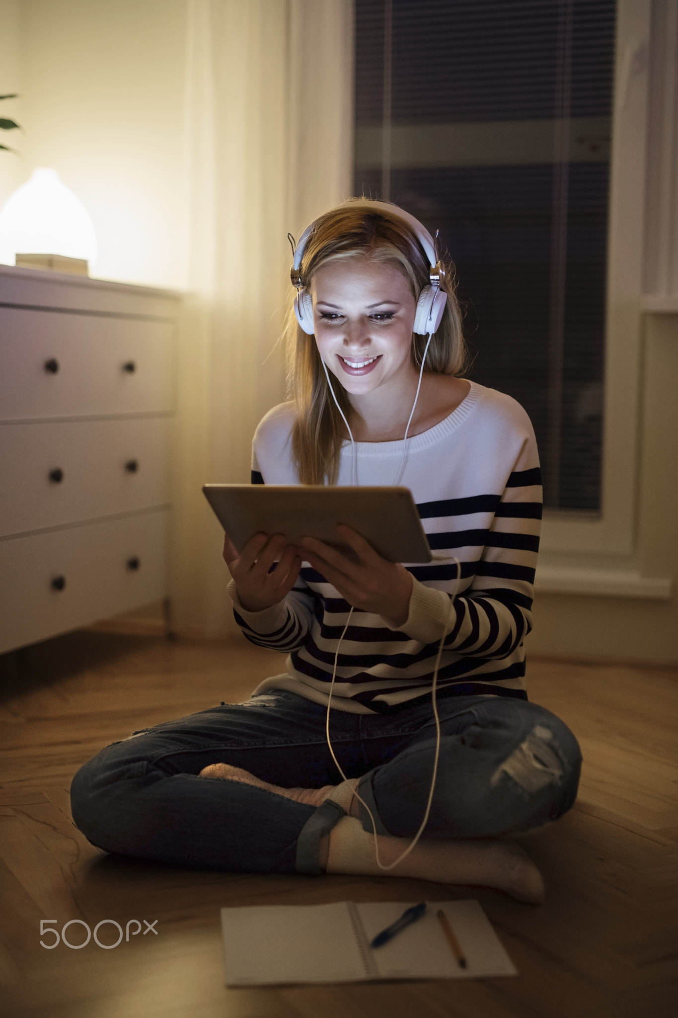 Woman sitting on the floor, working on tablet at night.