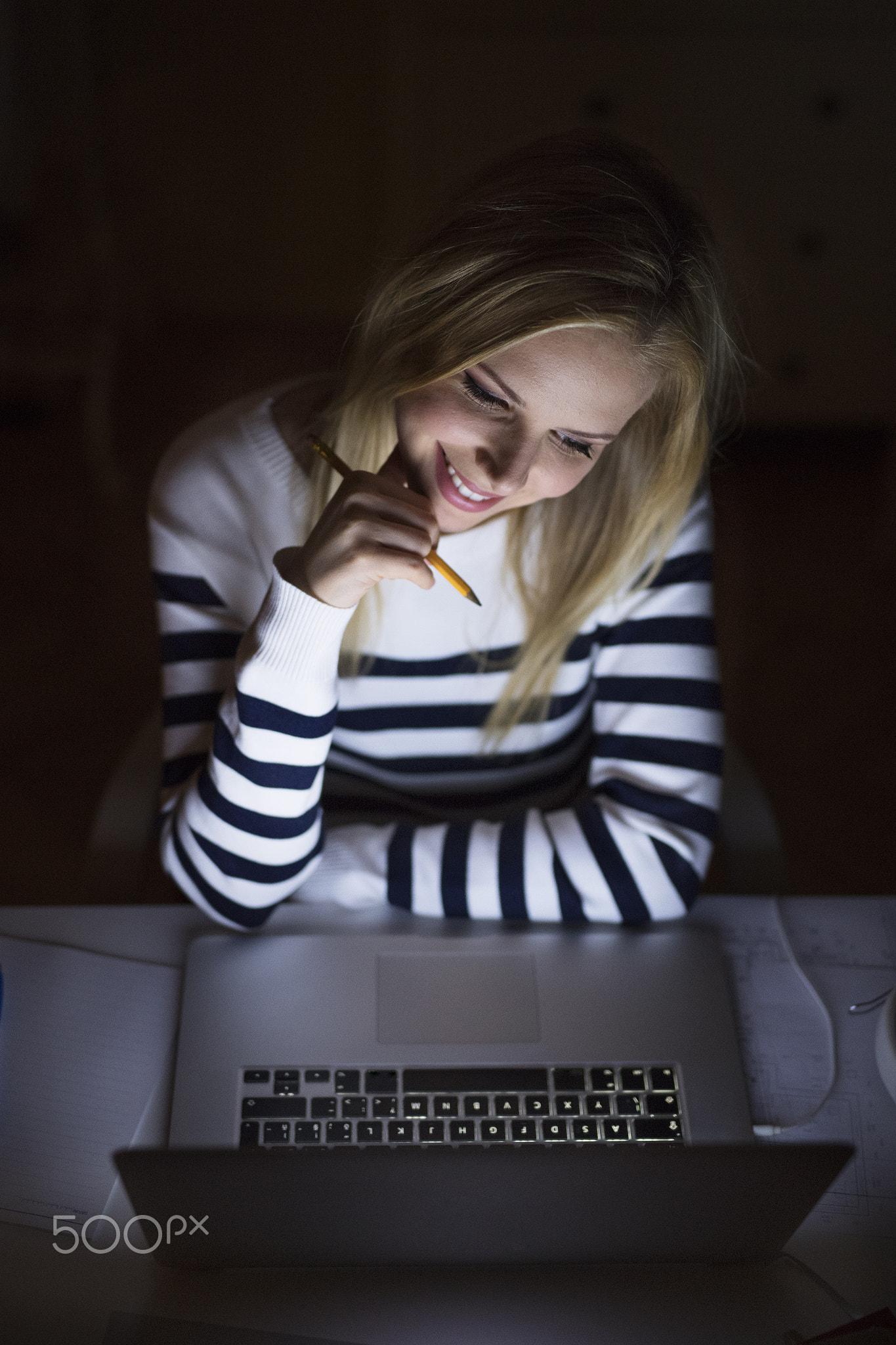 Woman sitting at desk and working on laptop at night.