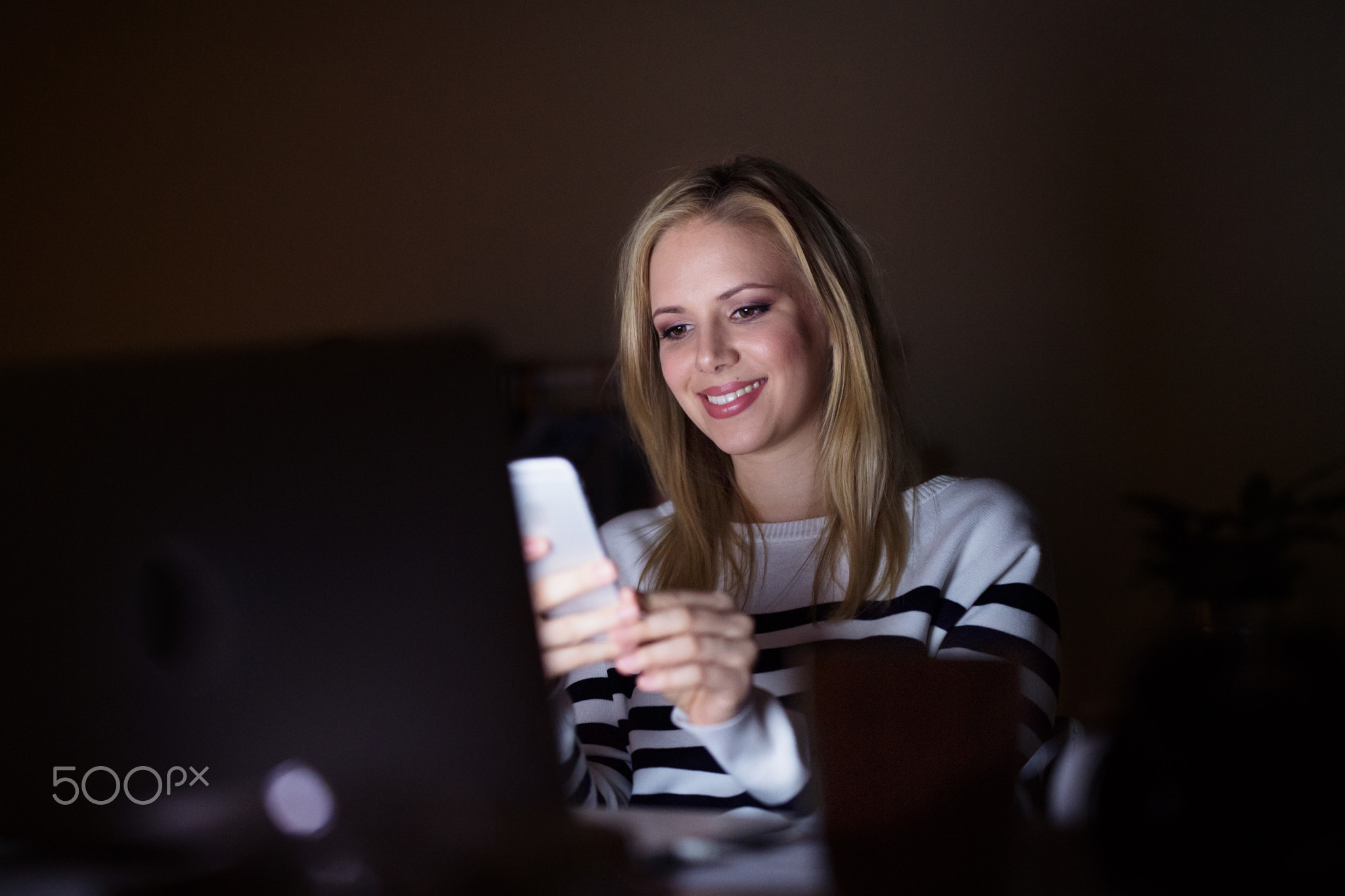 Woman with laptop and smartphone, texting.
