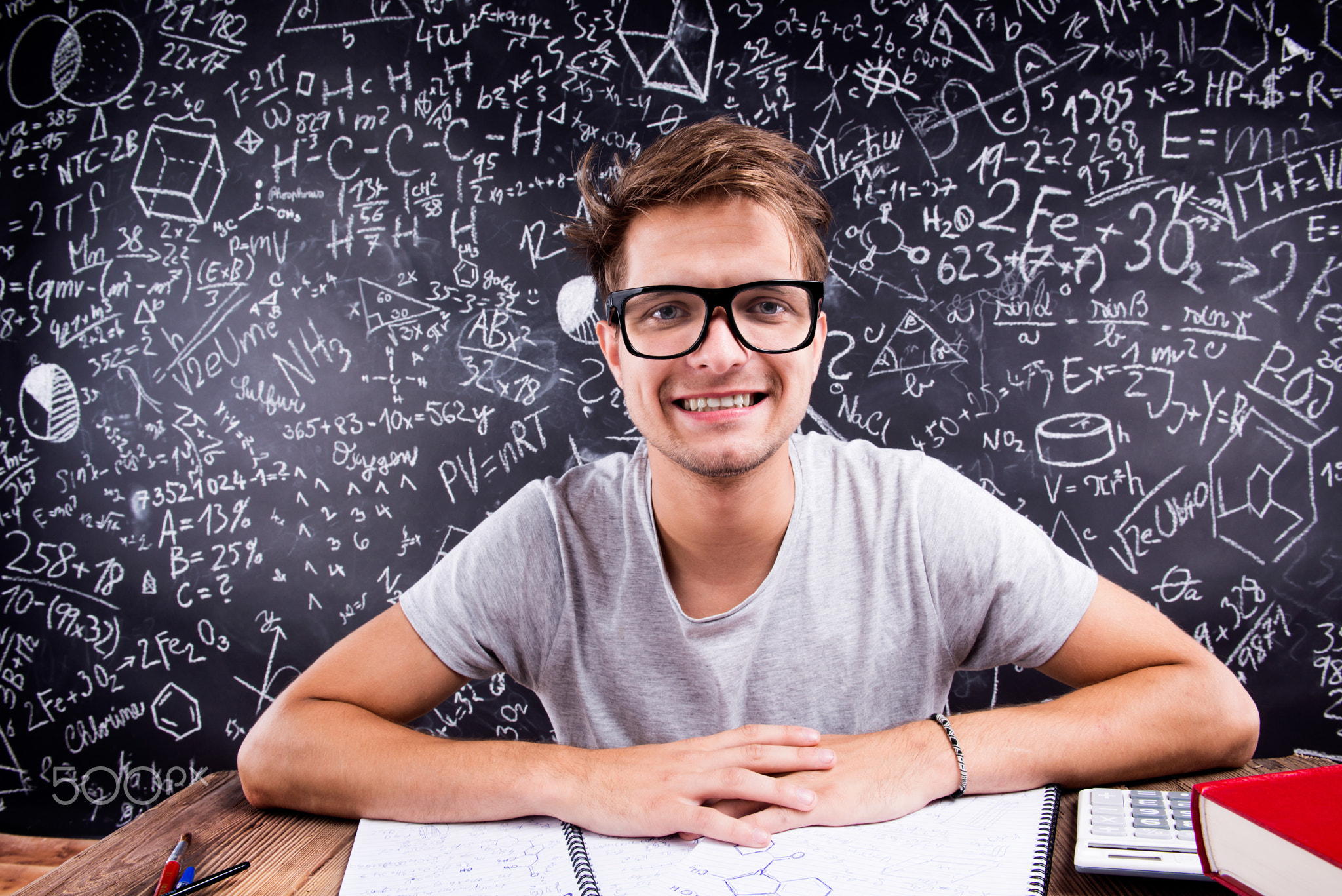 Hipster student doing his homework against a big blackboard
