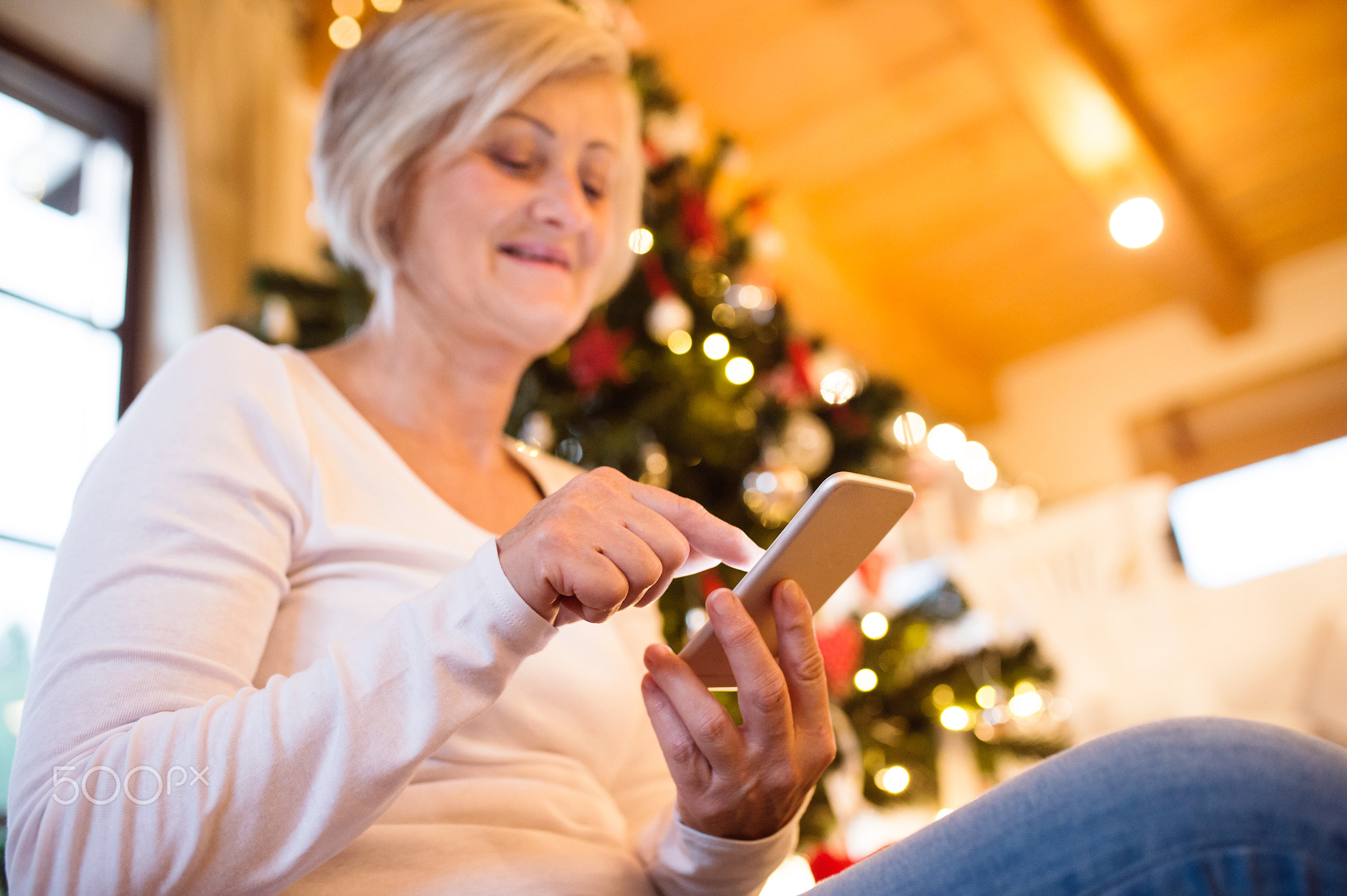 Senior woman with smartphone in front of Christmas tree.