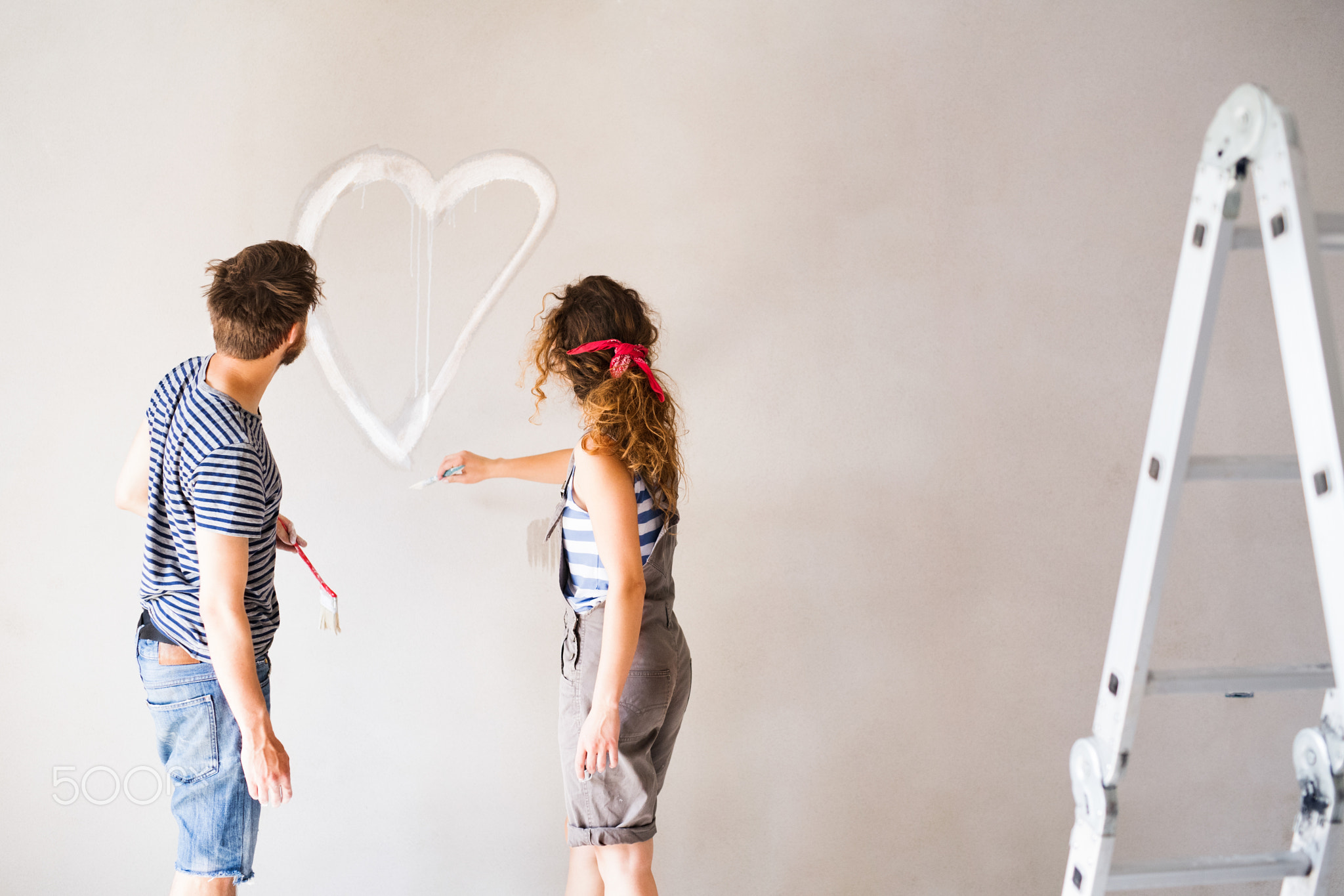 Couple painting heart on the wall in their house.