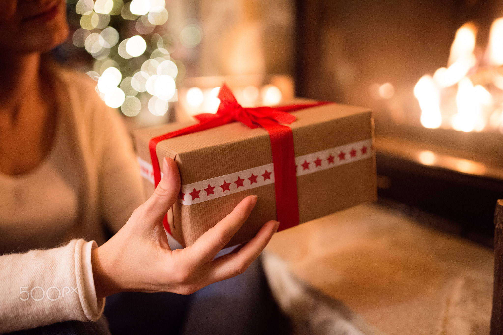 Unrecognizable woman in front of Christmas tree giving present