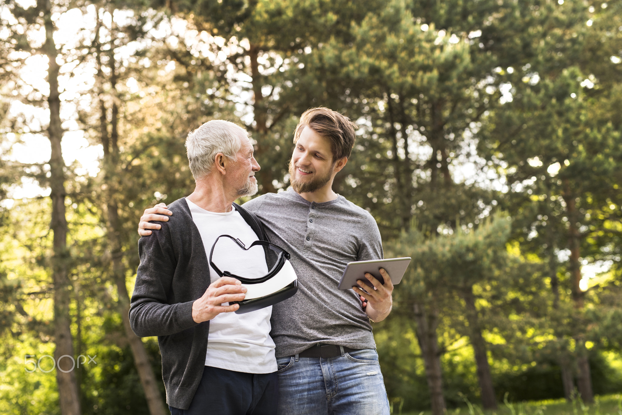 Young man and his senior father with VR glasses outdoors.