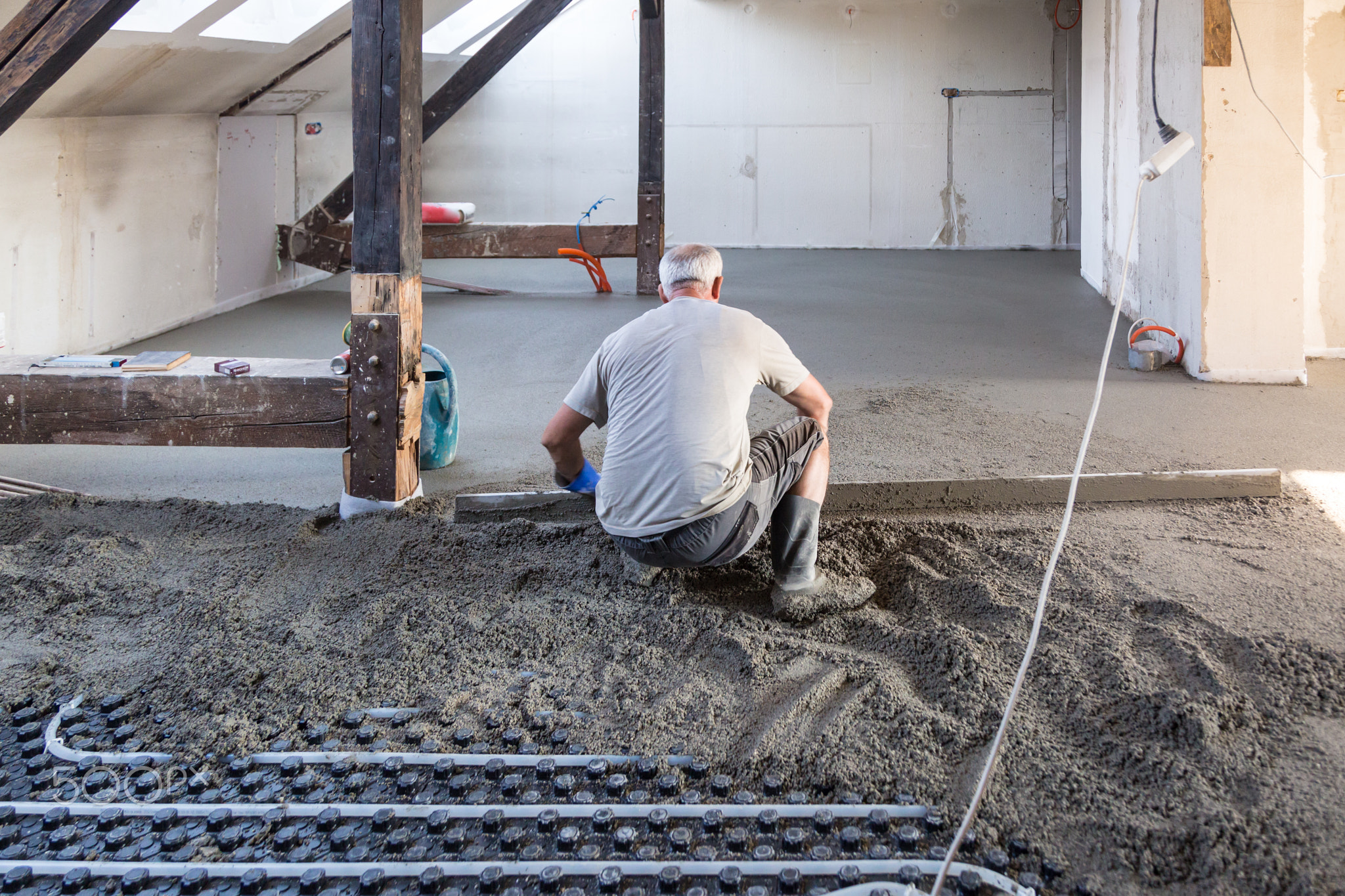 Laborer leveling sand and cement screed over floor heating.