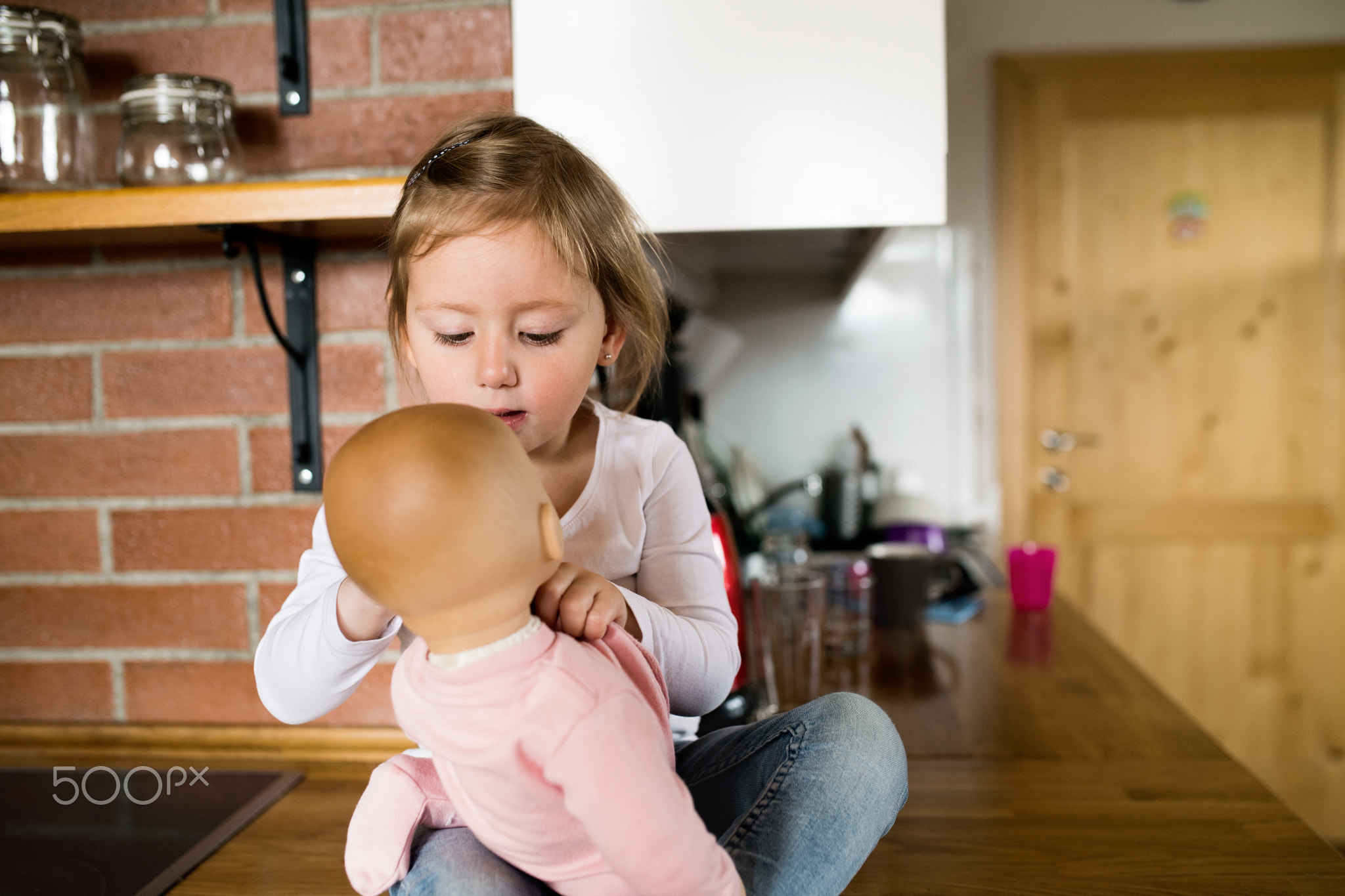 Cute little girl with her doll sitting on kitchen countertop